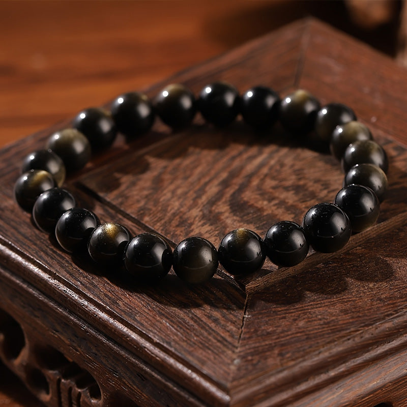 Bracelet styled on carved wooden surface, combining golden obsidian and black agate beads to evoke grounded energy, protection, and timeless elegance.