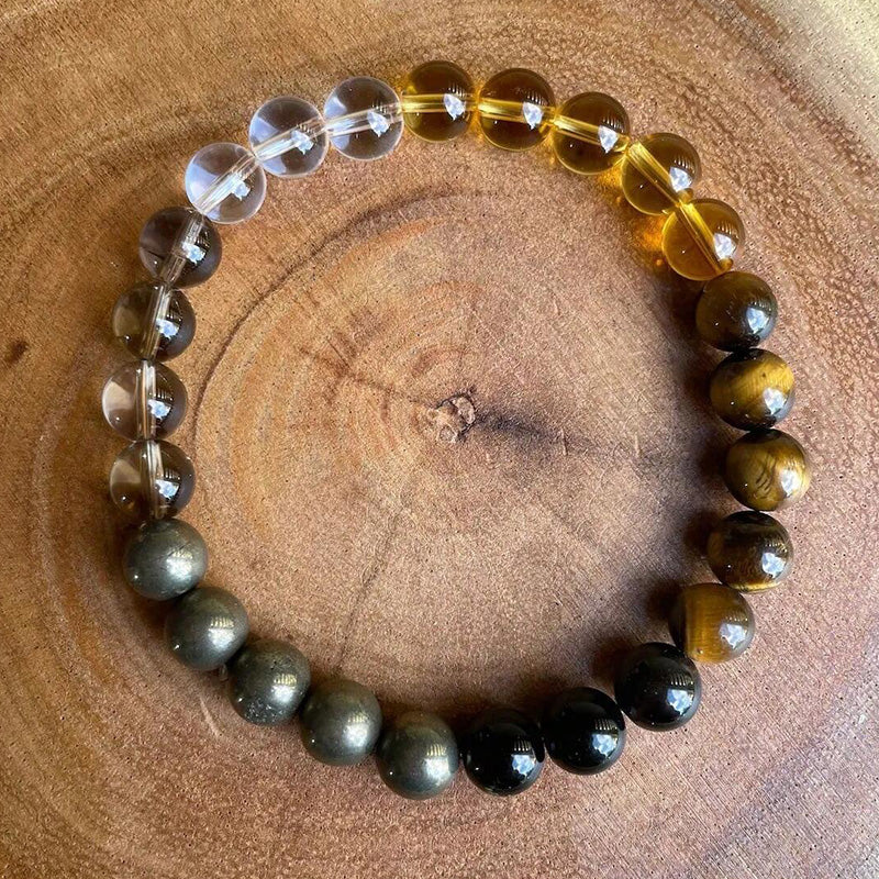 Bracelet arranged in a circle on a wooden surface, featuring golden tiger’s eye and dark obsidian beads with smoky quartz and clear stones for a grounded, natural presentation.