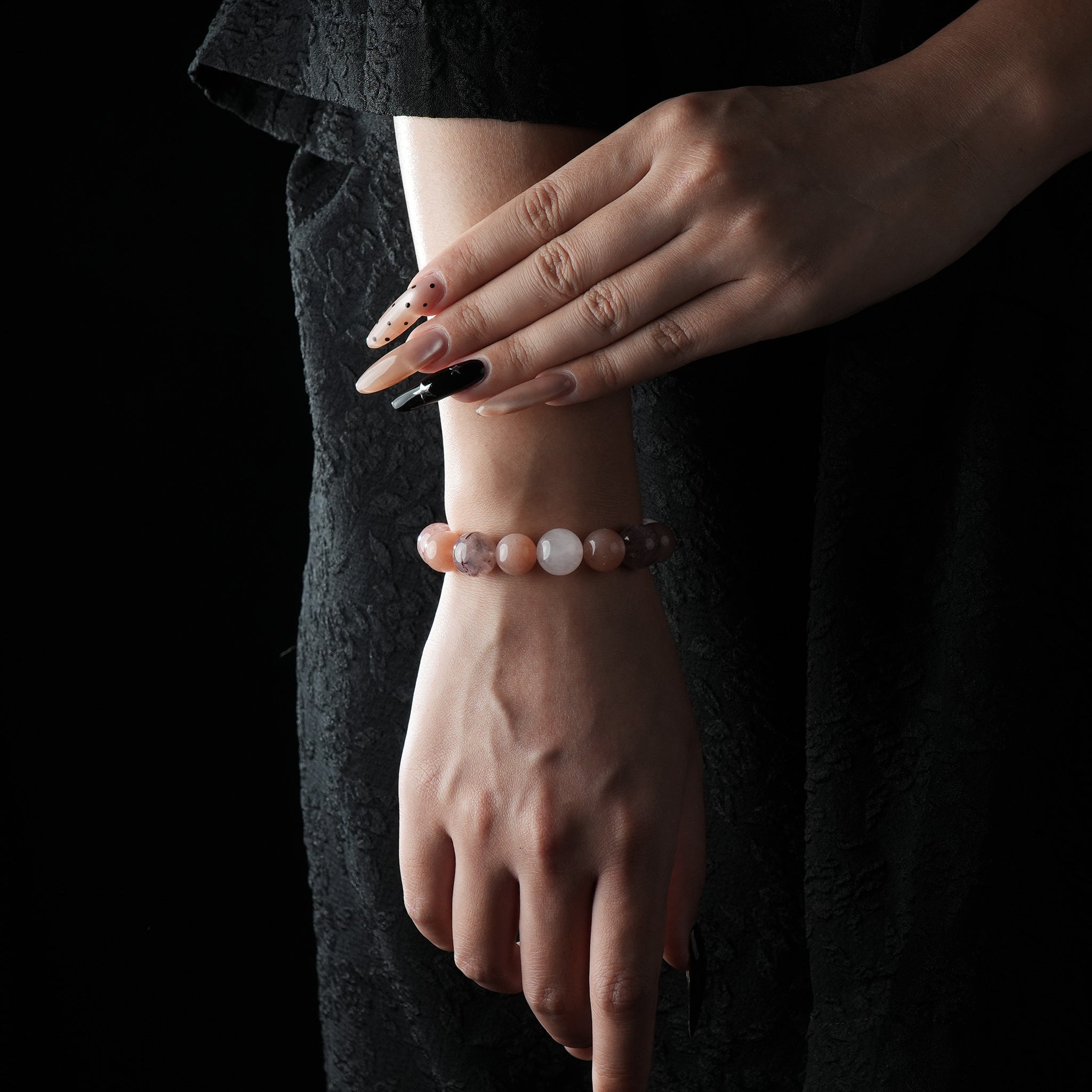 A beaded bracelet featuring orange moonstone, rose quartz, and strawberry quartz, worn on the wrist against a black outfit backdrop.