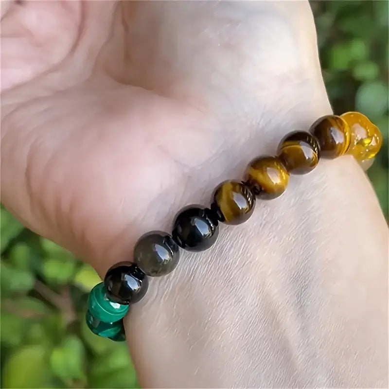 A beaded crystal bracelet worn outdoors, catching natural light to highlight the golden and green hues of the stones.