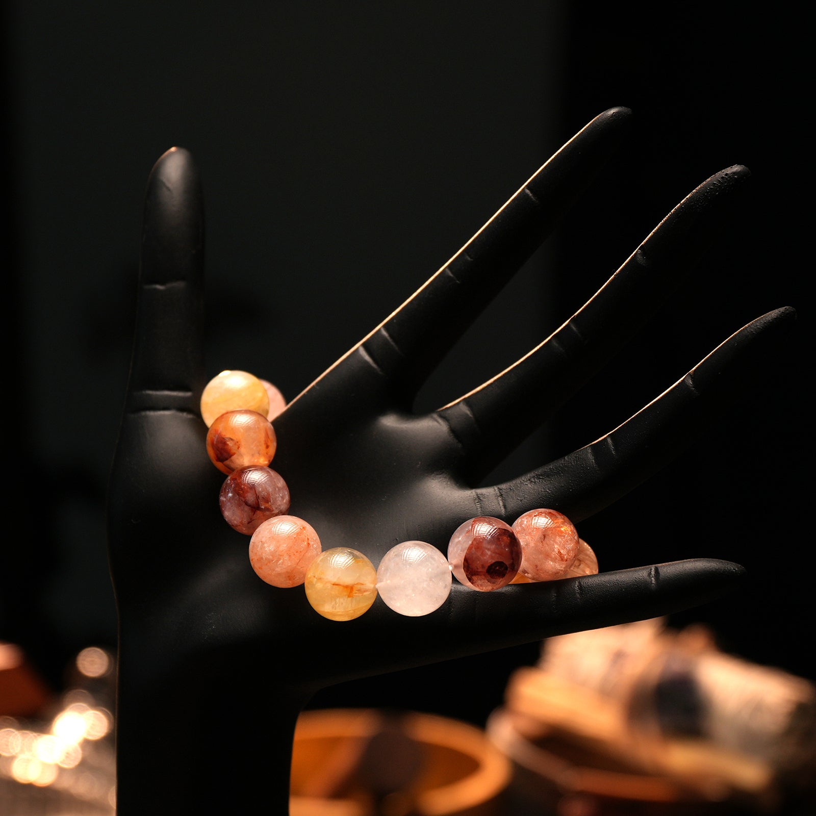 Bracelet laid across mannequin fingers, with beads in soft gradients of amber, gold, and crimson tones, representing inner fire and focus.