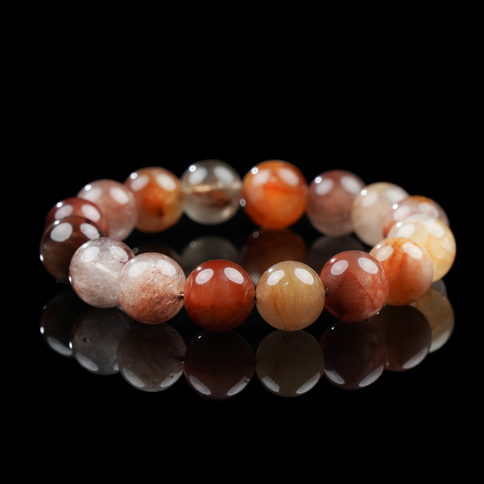 A close-up of a red hematoid quartz bracelet resting on a glossy black surface, showcasing the variation of deep red to amber hues in each polished crystal bead.
