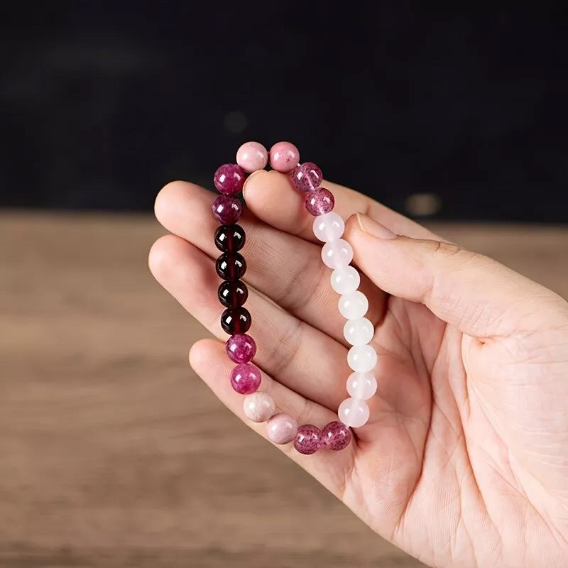 A hand holding the bracelet with visible garnet, rose quartz, and strawberry quartz beads, highlighting its blend of nurturing and empowering energies.