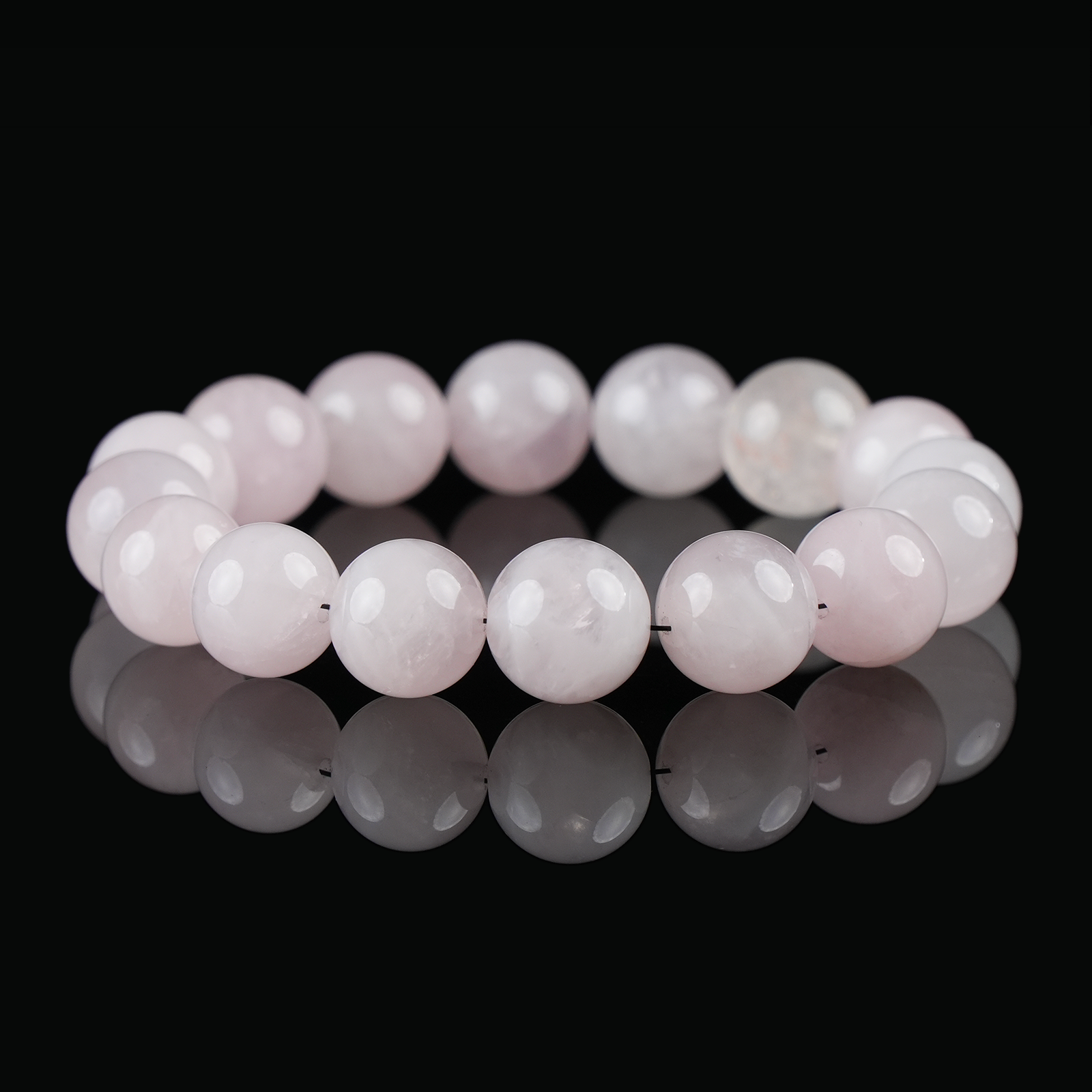 Flat lay of rose quartz crystal bracelet with soft pink polished round beads, displayed on a glossy black background.