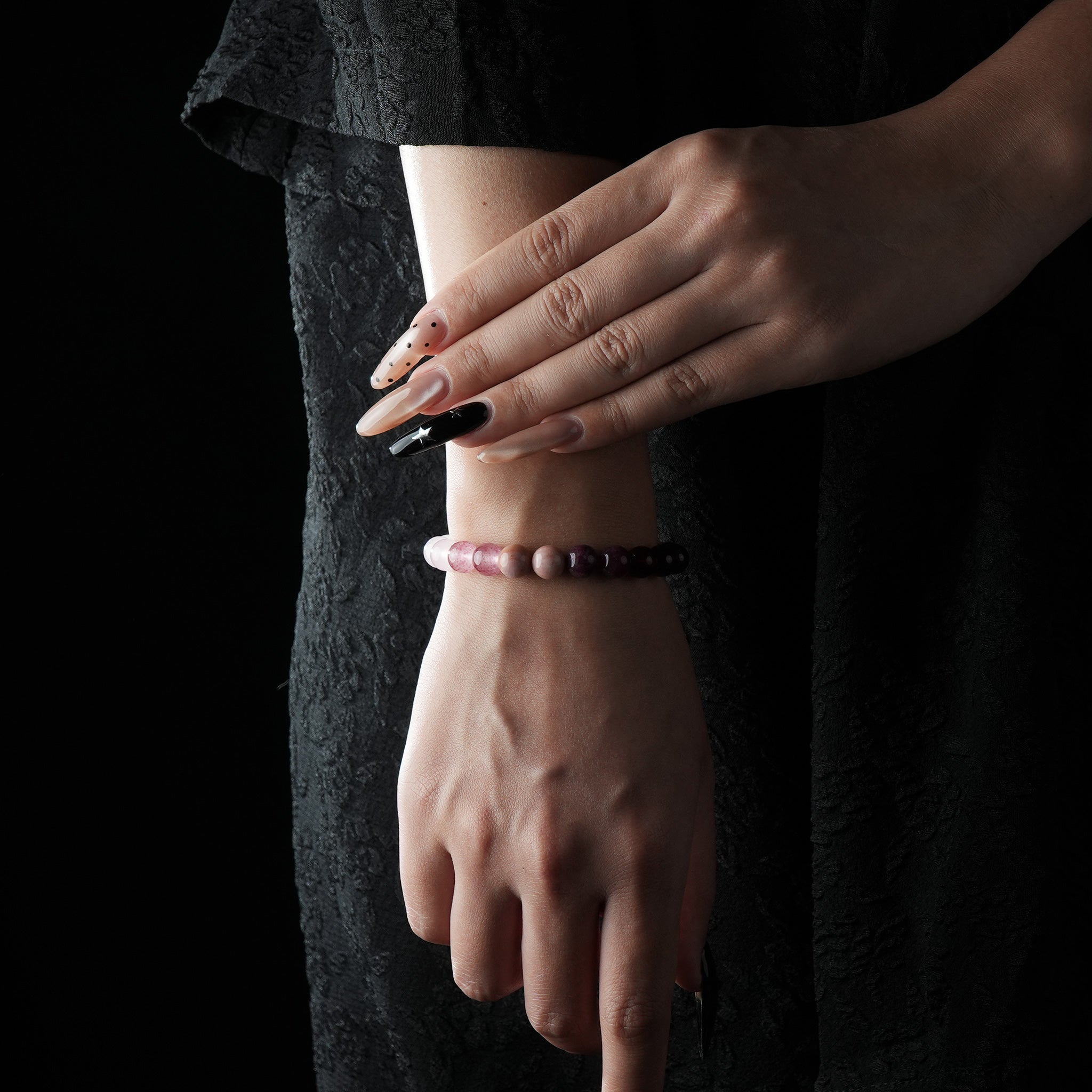 A bracelet featuring rose quartz, strawberry quartz, and garnet beads, worn on the wrist against a black lace outfit.