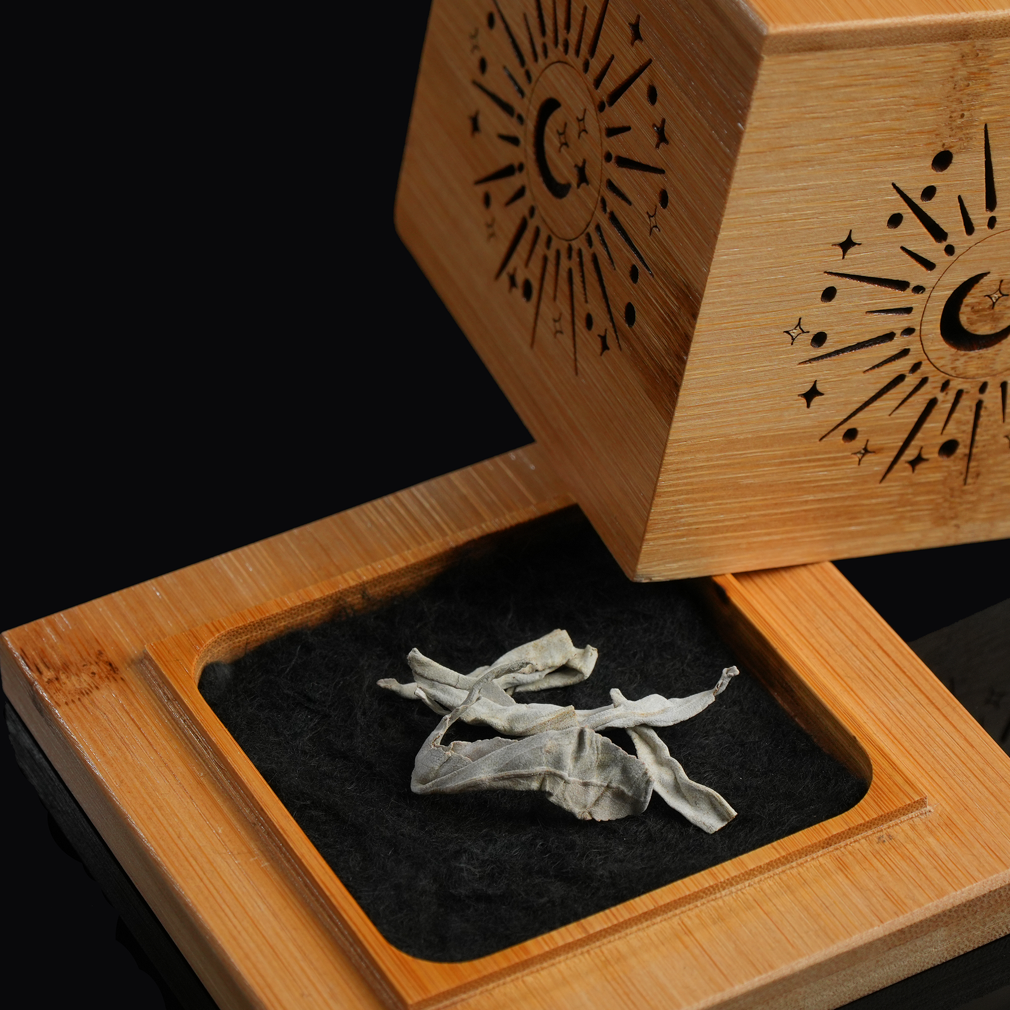 Open bamboo smudge box revealing white sage bundle inside, lid propped back, black backdrop.