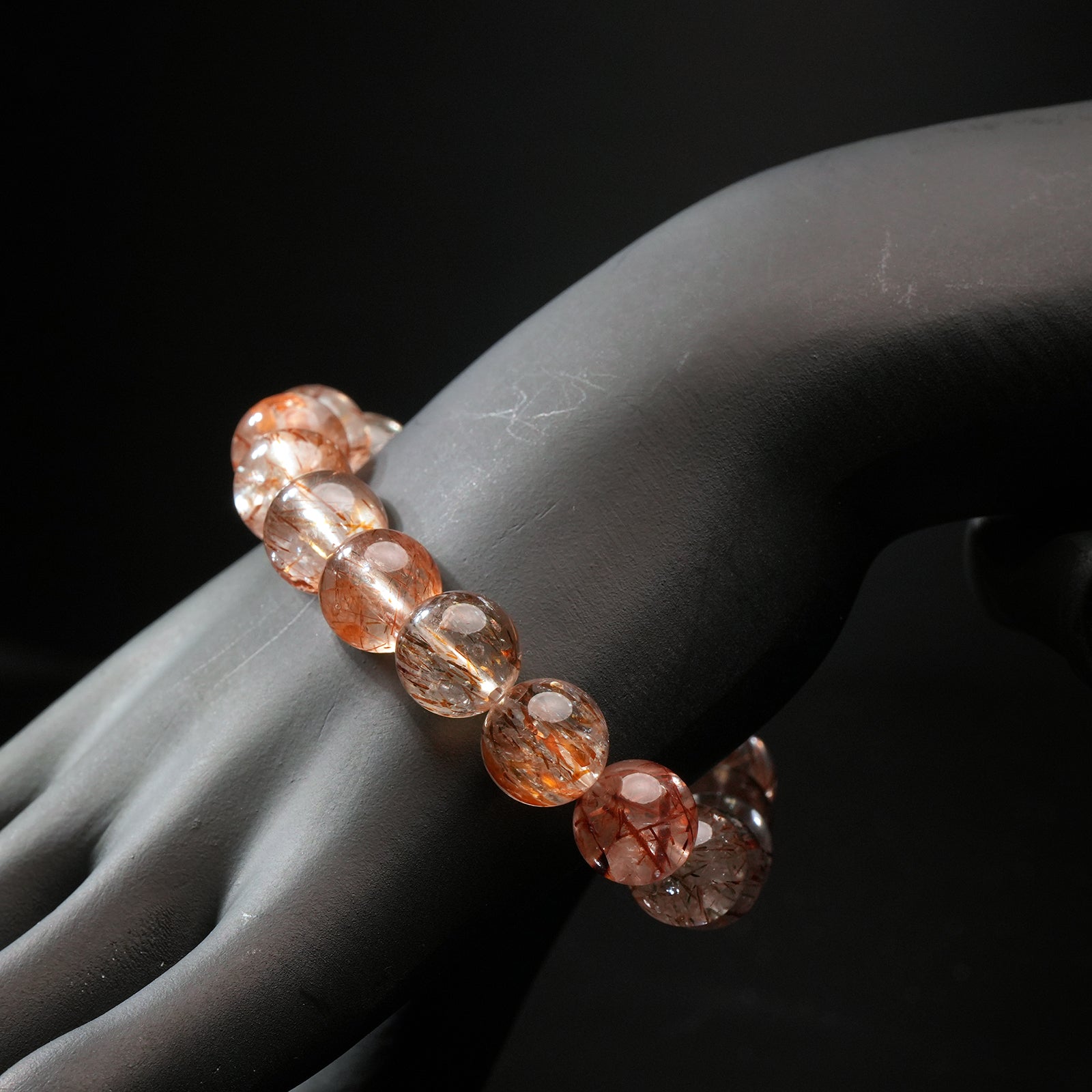 Side angle of red rutilated quartz bracelet worn on a mannequin wrist, highlighting transparency and vivid inclusions.