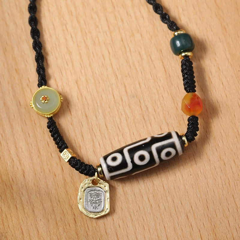 The Tibetan 9-eye agate Dzi bead necklace on a wooden background, showcasing its intricate beadwork and gold charm detail.