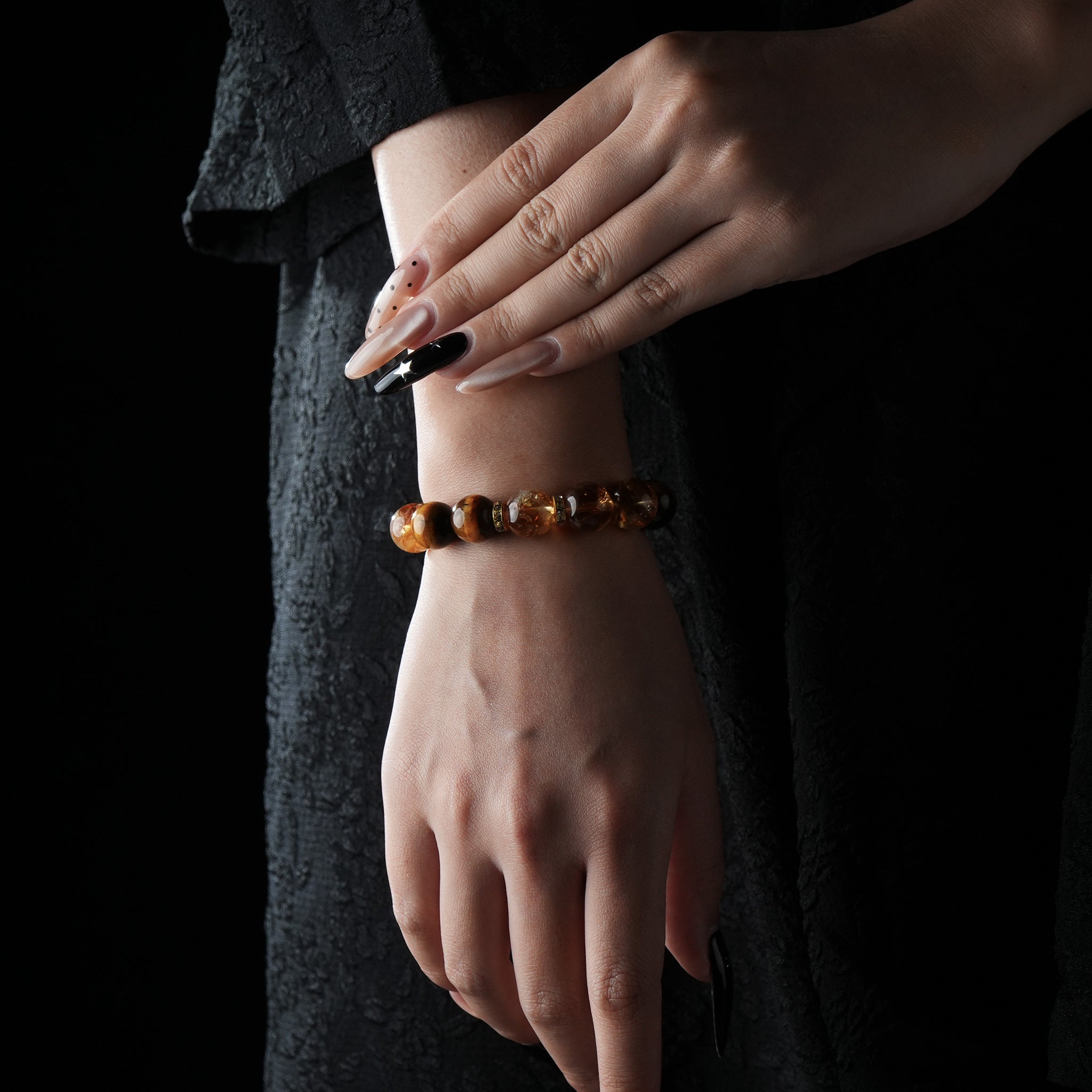Elegant bracelet made of polished Tiger’s Eye, Citrine & Clear Quartz Bracelet,worn on a wrist against a black textured dress background.