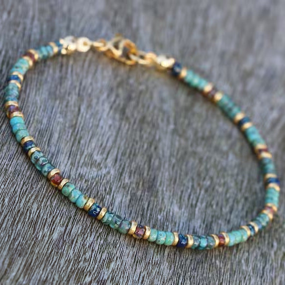 A turquoise beaded anklet with golden clasp laid flat on a gray wood surface.