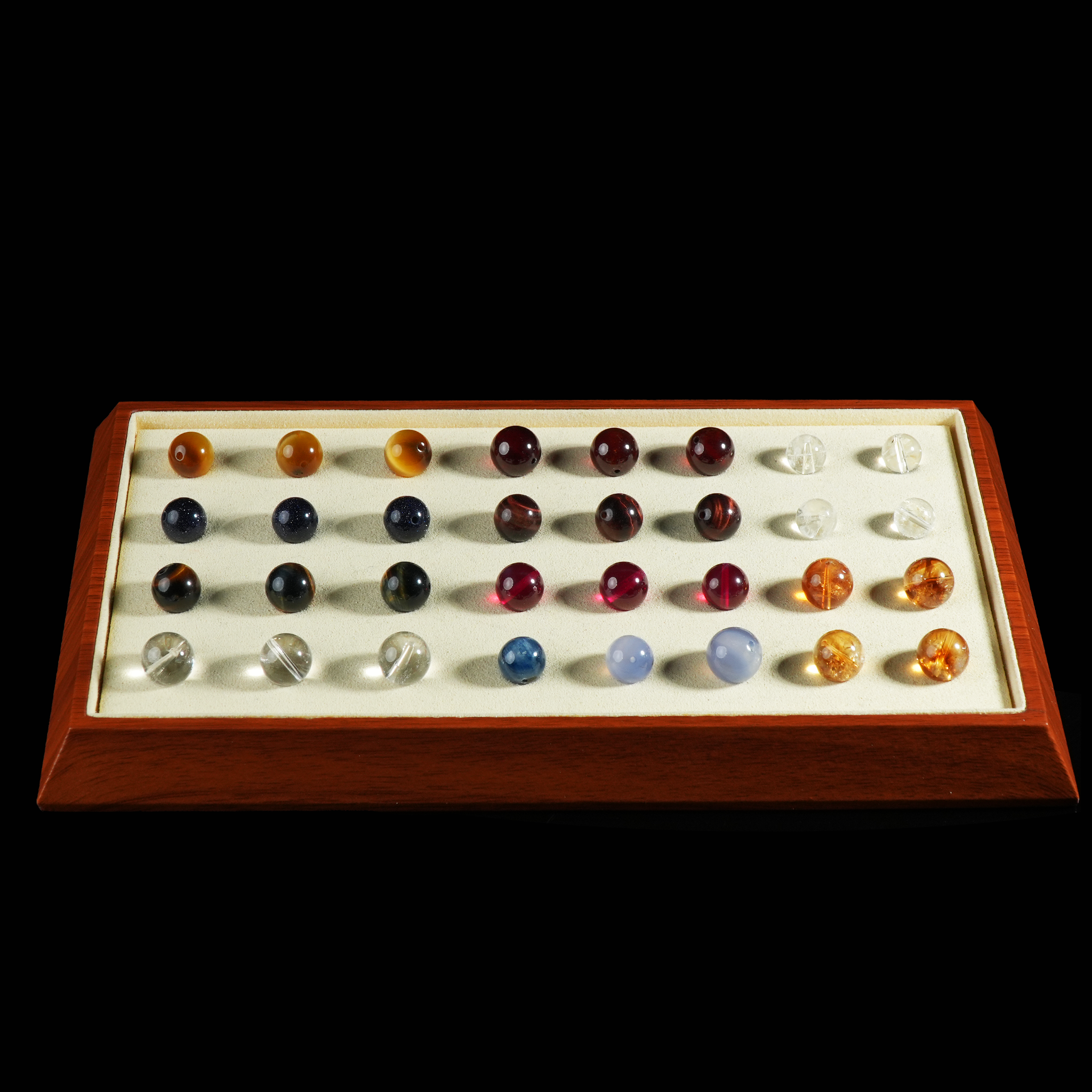 The display tray is filled with various colored gemstone beads, each placed in an individual indentation. The contrast between the vibrant stones and the soft cream velvet creates a visually appealing and organized presentation.