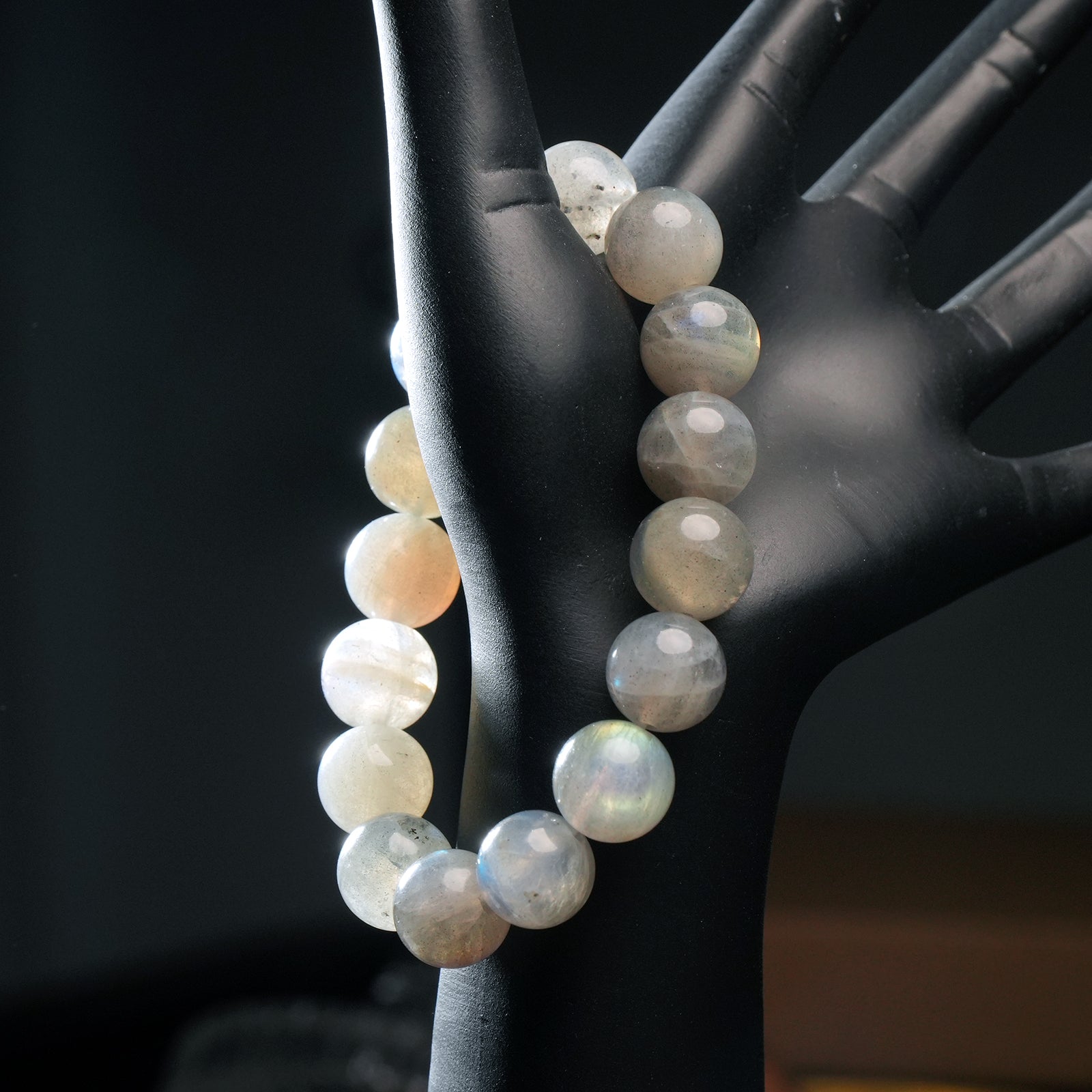 Gray moonstone crystal bracelet worn on mannequin hand, reflecting gentle inner glow and subtle shimmer under light.