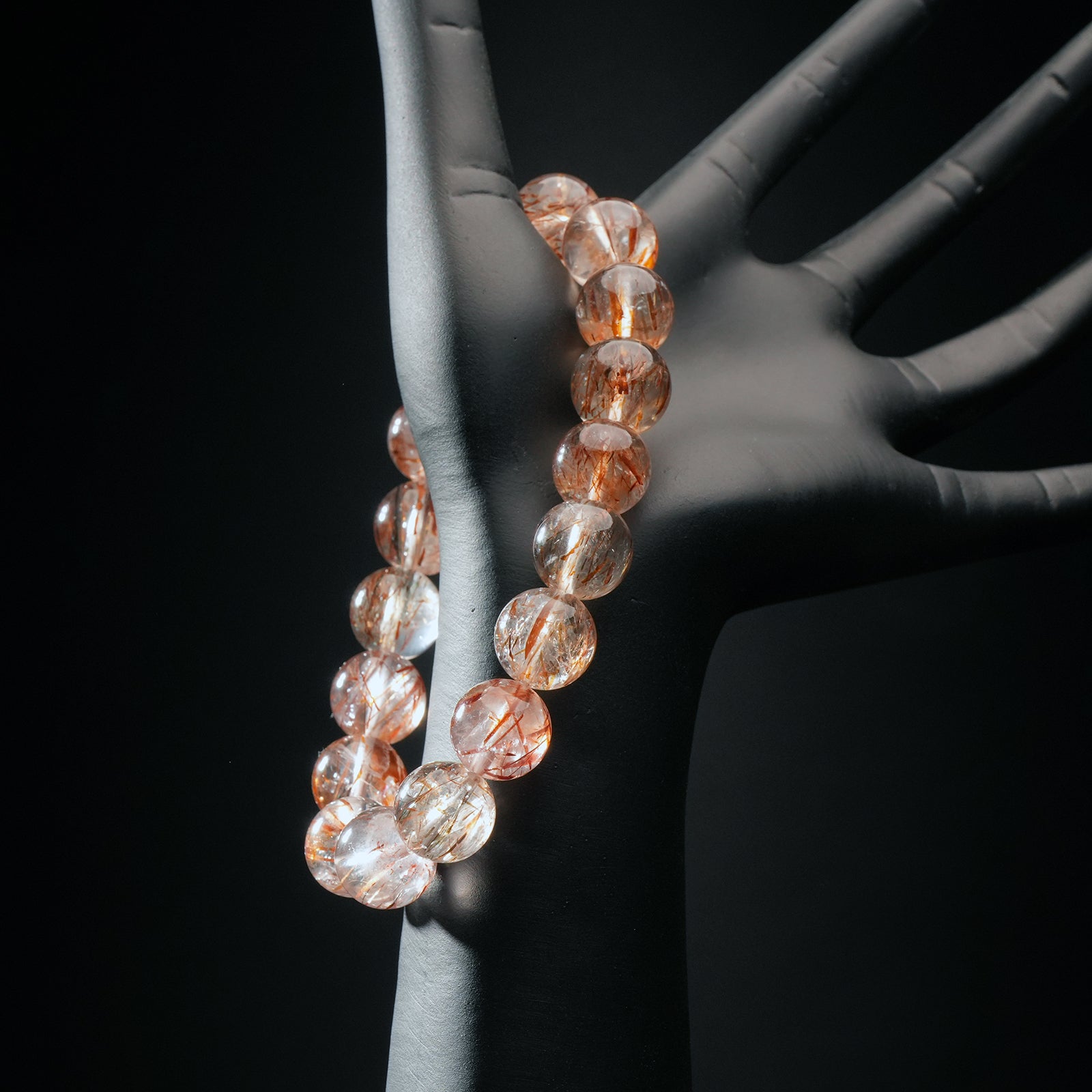 Red rutilated quartz crystal bracelet worn on a mannequin hand, showcasing clear beads with striking red rutile threads.