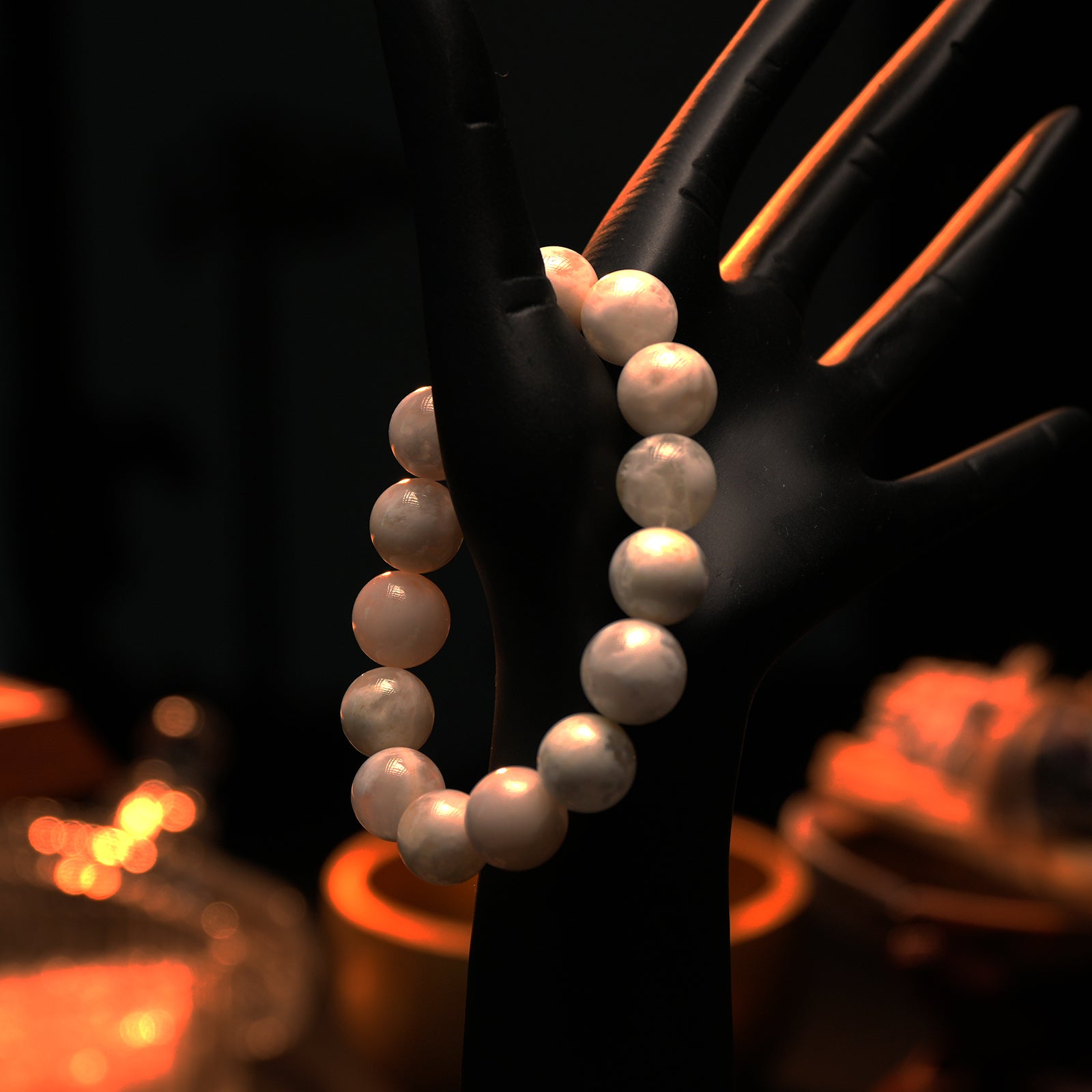 A hand mannequin displays the snow phantom quartz bracelet against warm ambient light, highlighting the soft glow of the white crystal beads.