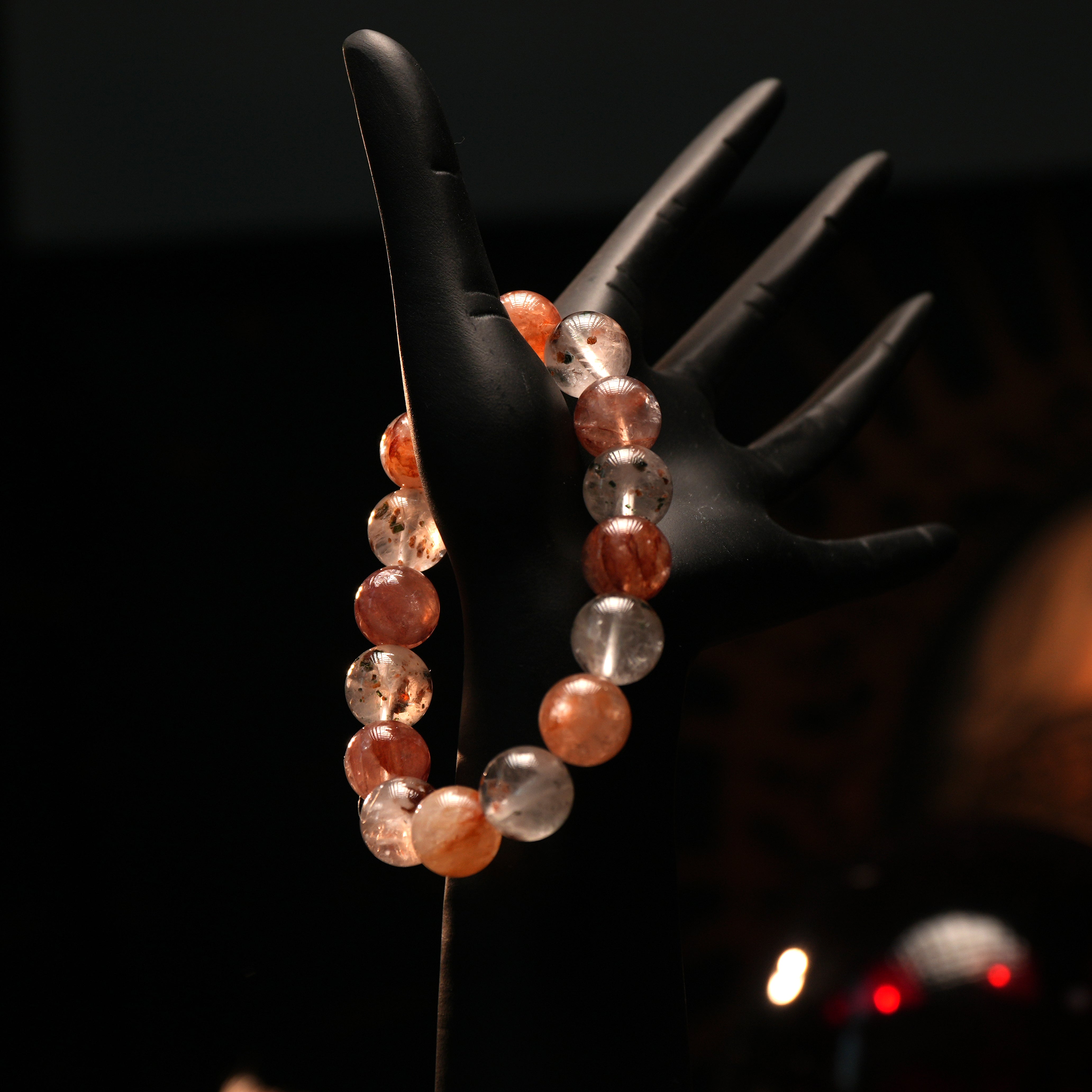 Bracelet modeled on hand stand in low light, showcasing shimmering red and pink quartz beads for emotional healing.