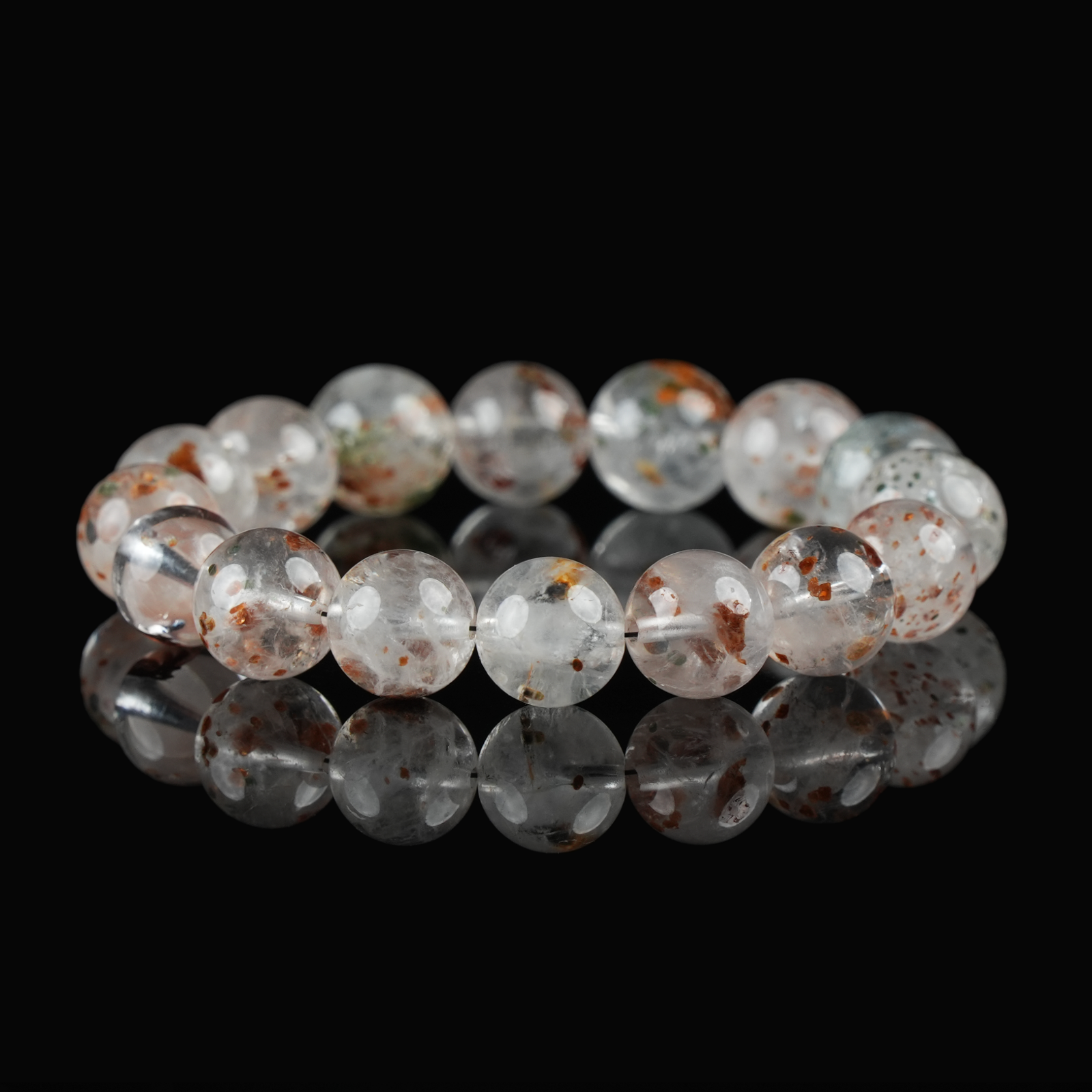 Flat lay of white phantom quartz bracelet featuring translucent beads with subtle red and green phantom inclusions on black reflective surface.