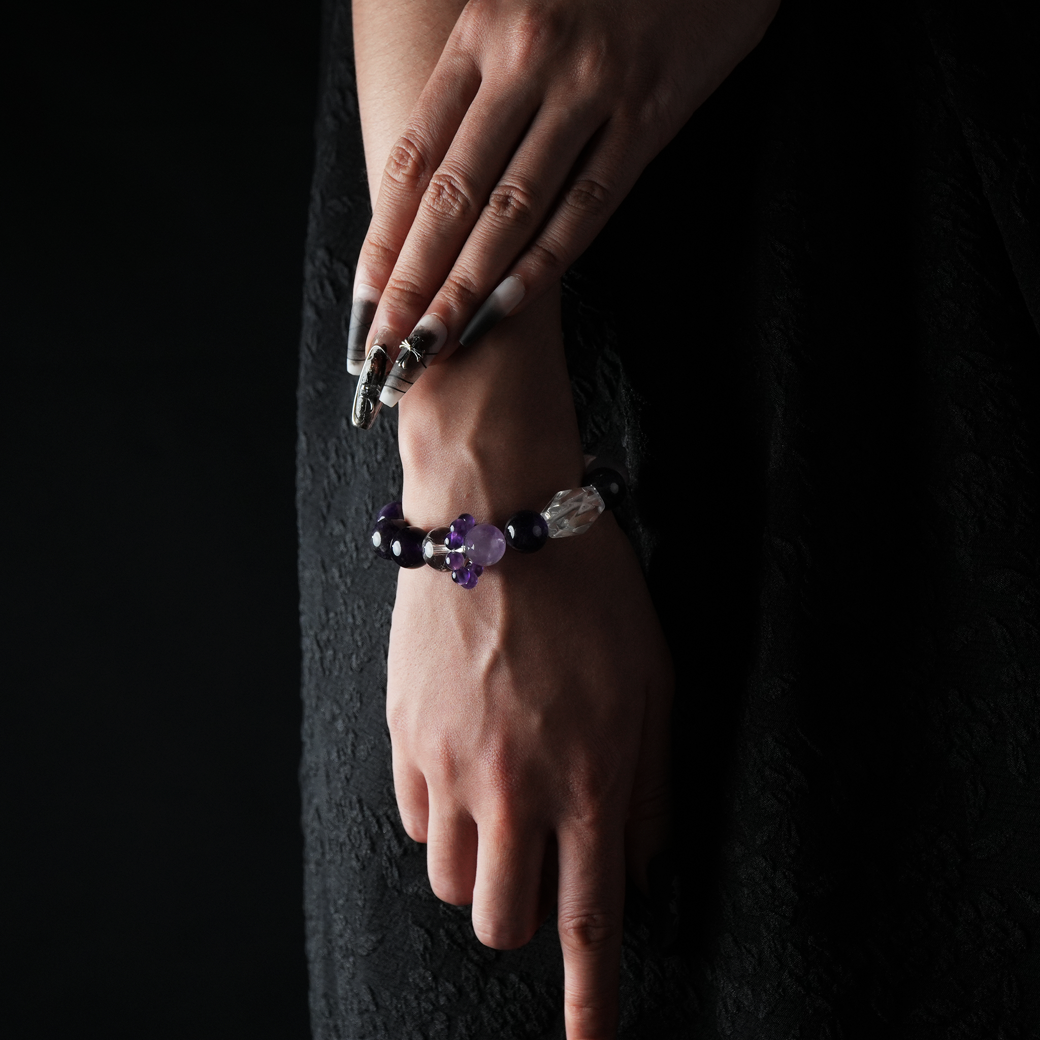 Close-up of a hand wearing a gemstone bracelet made of amethyst, clear quartz, and strawberry quartz, styled with elegant black clothing.