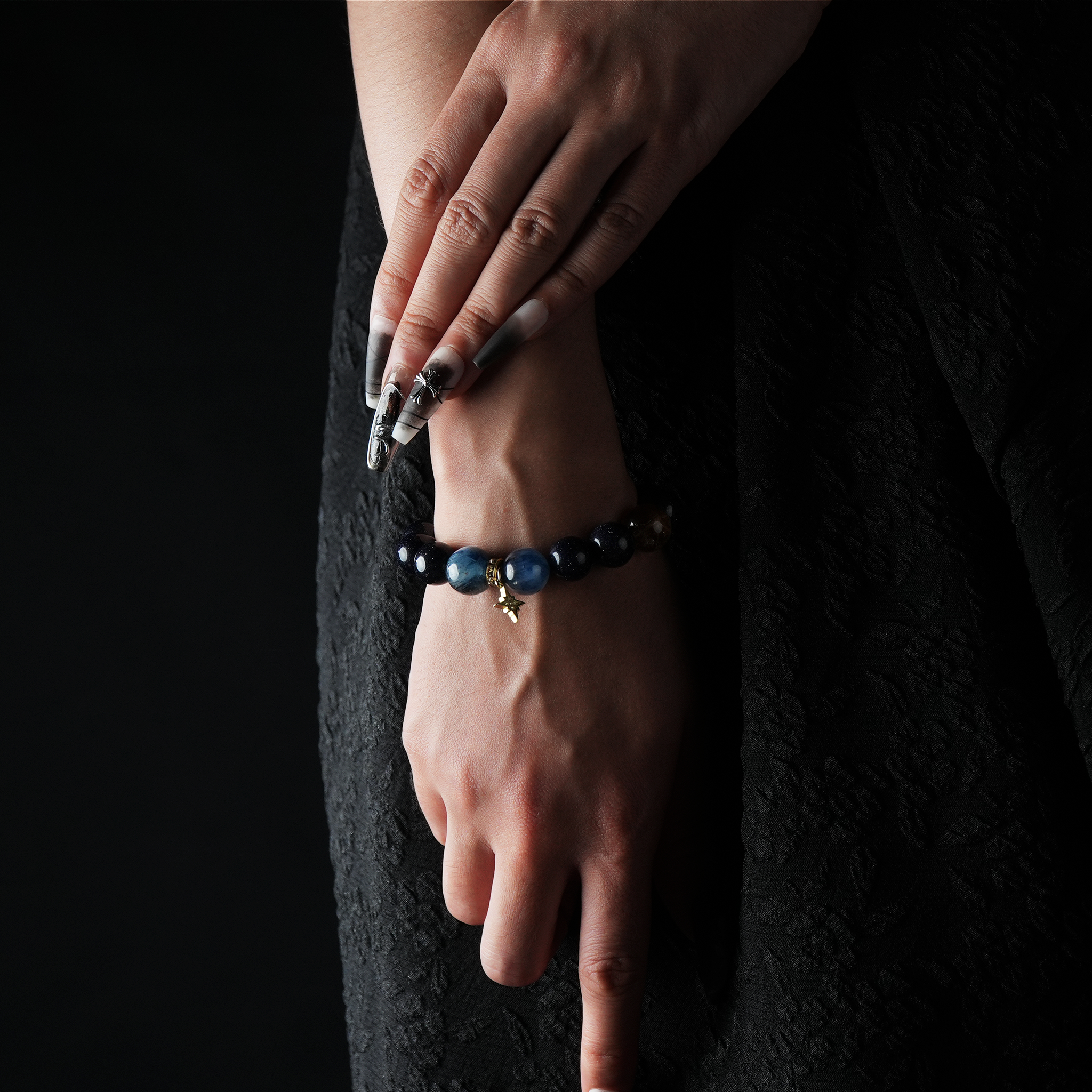 Woman wearing a bracelet made of aquamarine, blue sandstone, and moonstone with a small gold charm, against a dark outfit.