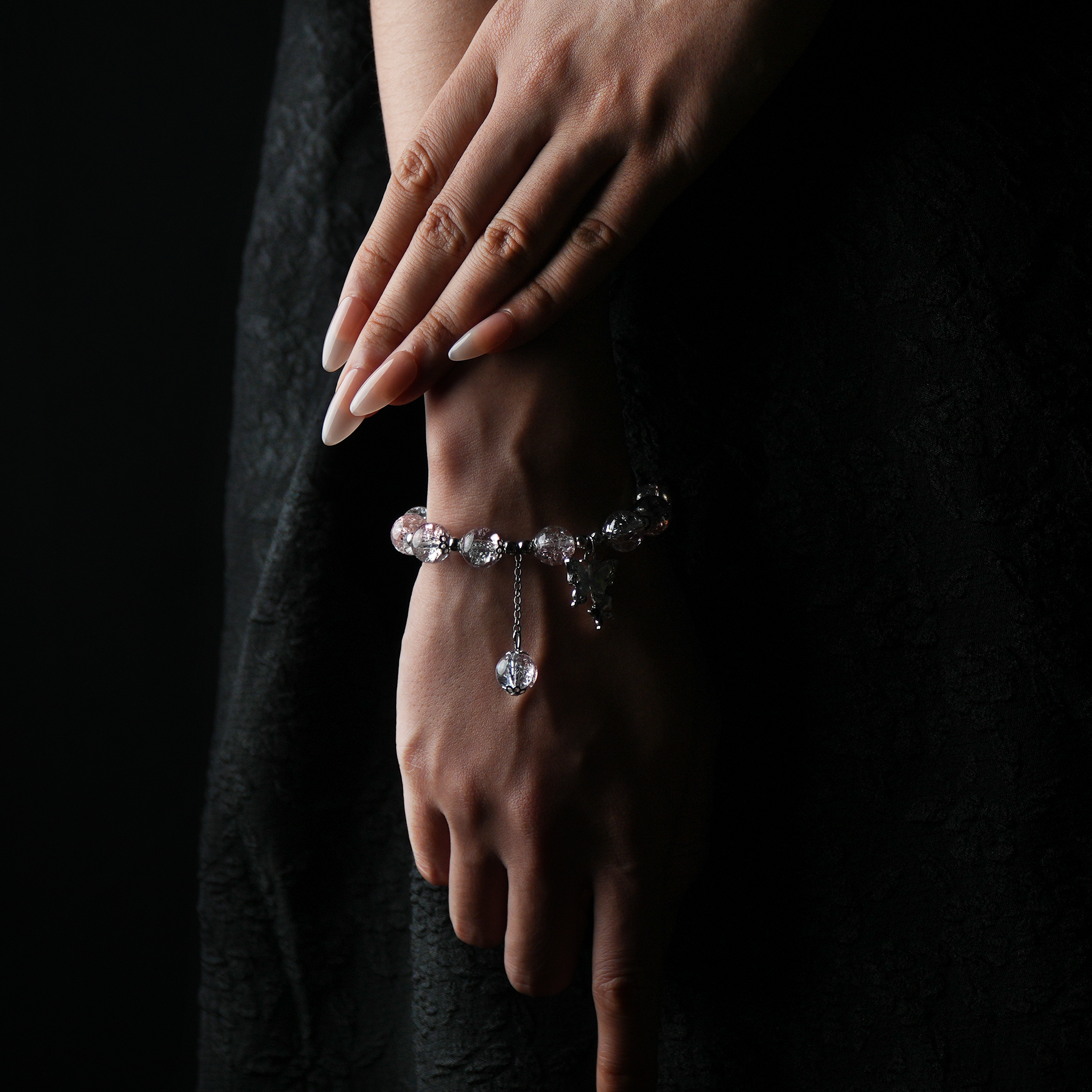 A wrist wearing a clear and blush-toned energy bead bracelet—delicate and luminous, with a butterfly charm that dances like a tiny fairy, enhancing its soft elegance.