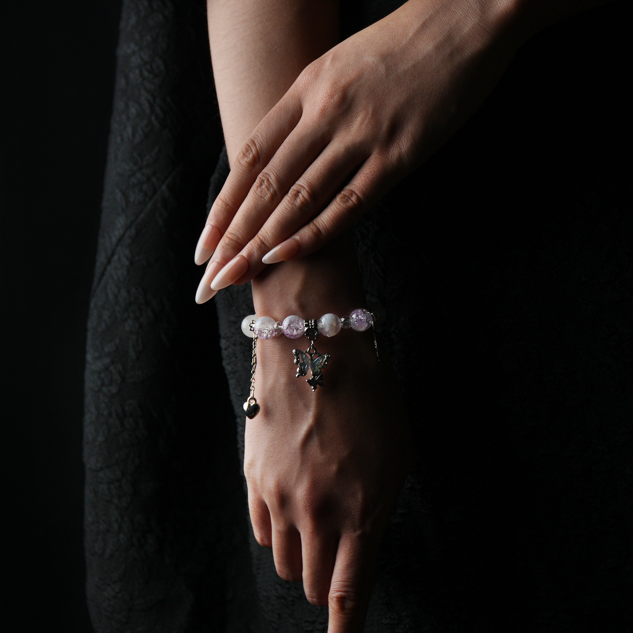 A wrist adorned with a pink and purple energy bead bracelet, softly shimmering with a silver butterfly charm—sweet, romantic, and full of graceful energy.