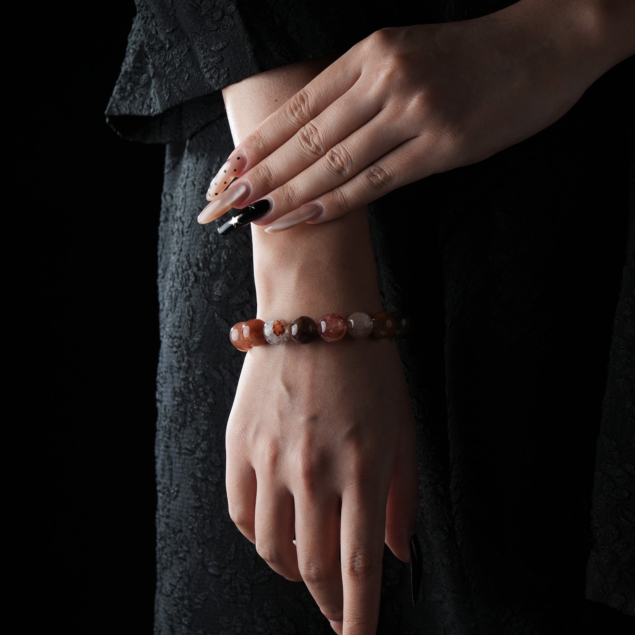 A red hematoid quartz crystal bracelet with warm reddish tones is worn on the wrist, styled against a black outfit to highlight the natural gemstone's color and polish.