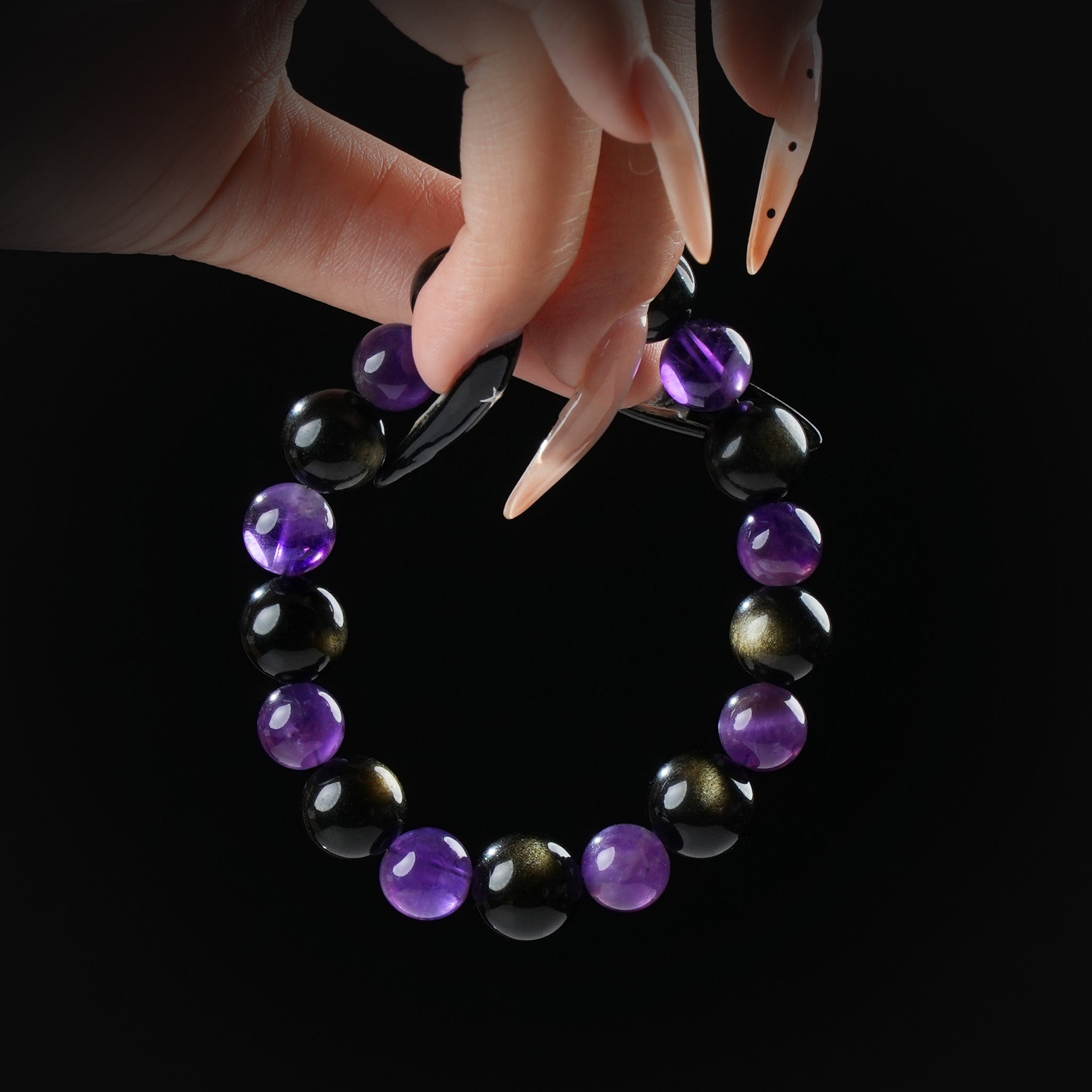 Amethyst and golden obsidian beaded bracelet held by hand on black background for protection and spiritual clarity.