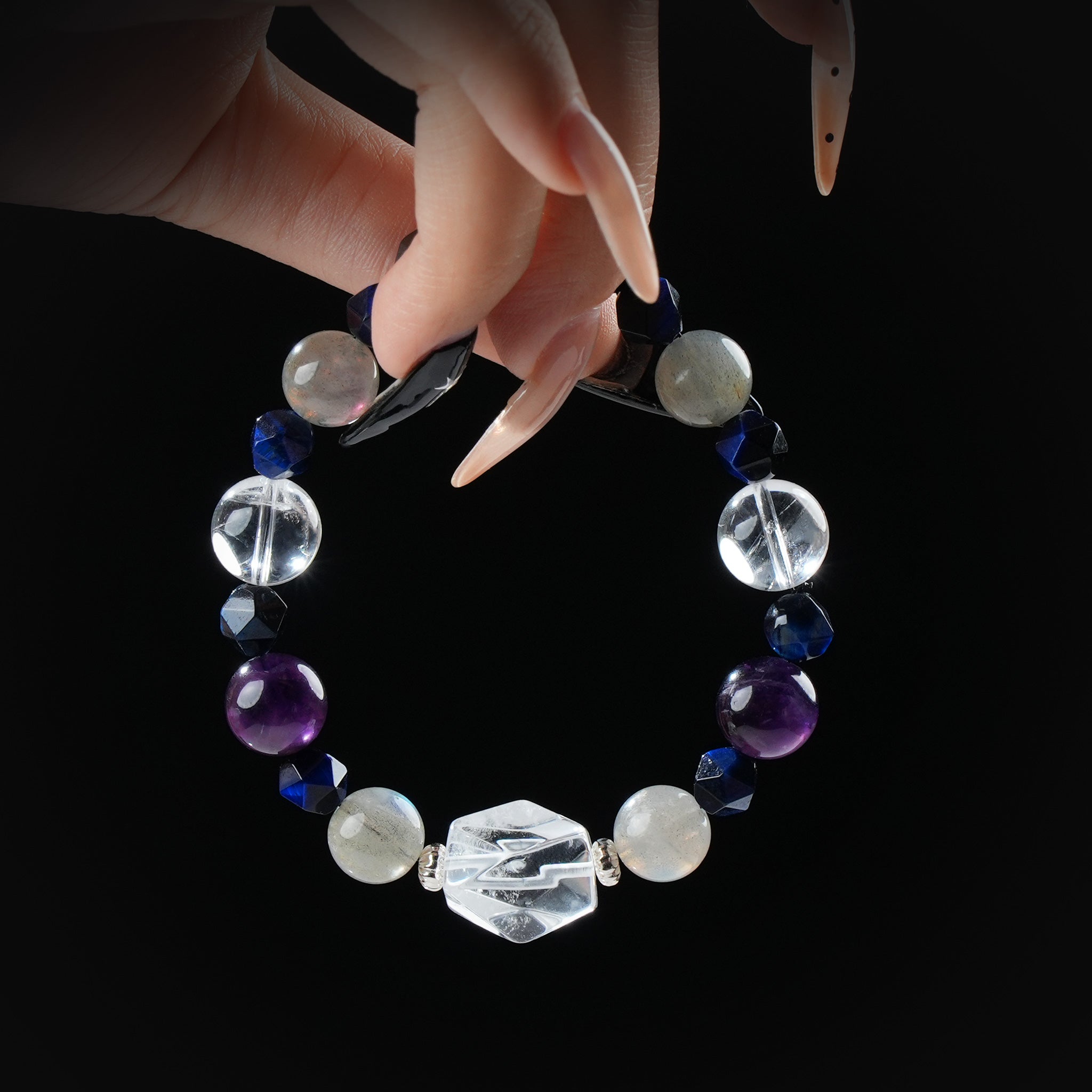 Amethyst, labradorite, lapis lazuli, and clear quartz bracelet with hexagon centerpiece, held by hand on black background for intuition and protection.