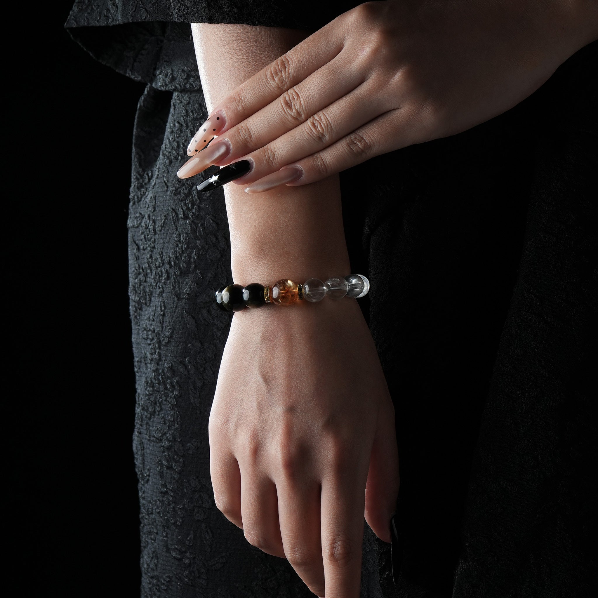 Stylish bracelet featuring black onyx, golden citrine, and clear quartz beads, worn on a wrist against a dark textured dress background.