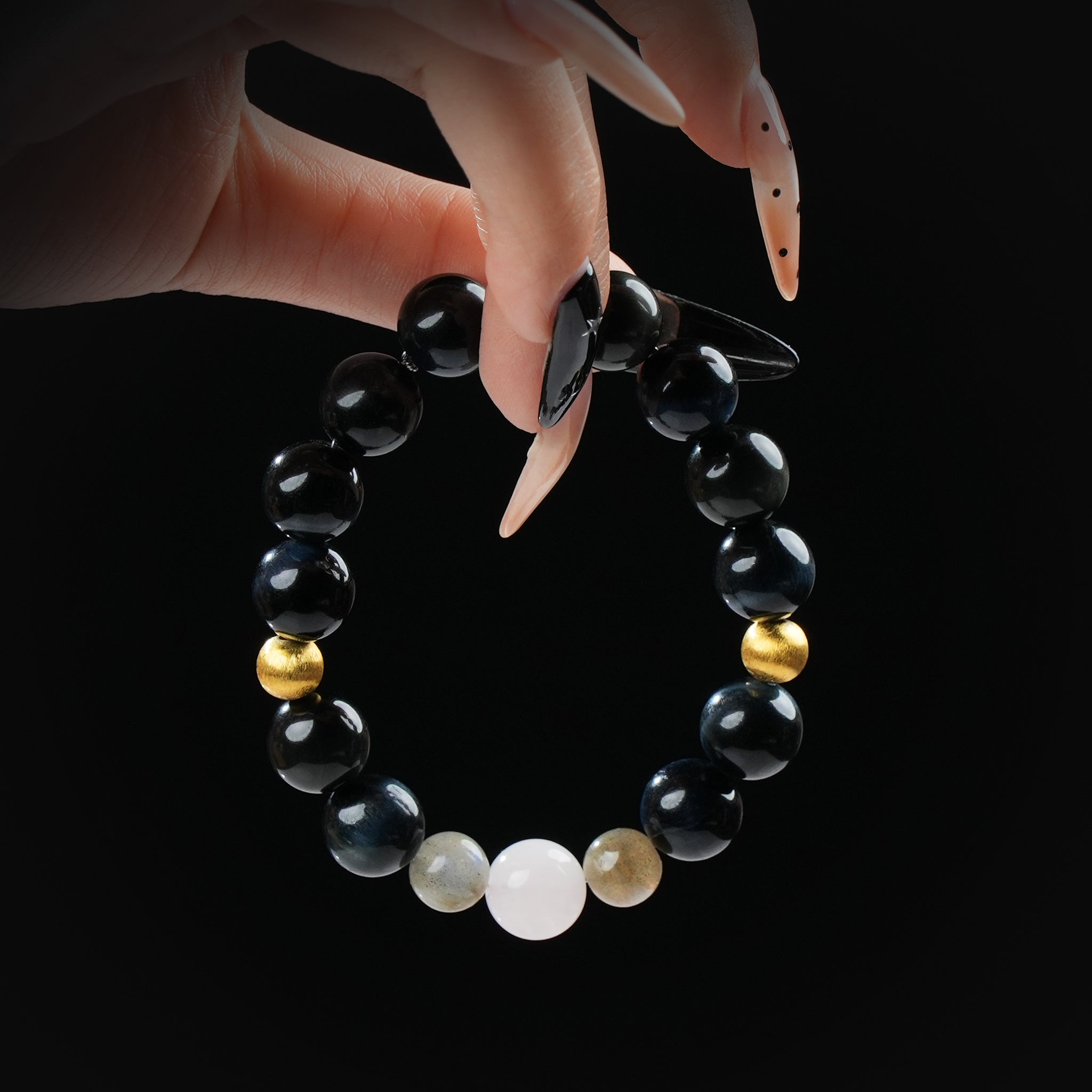 Black obsidian bracelet with gold hematite and white moonstone beads, held by hand on black background for a powerful and protective look.