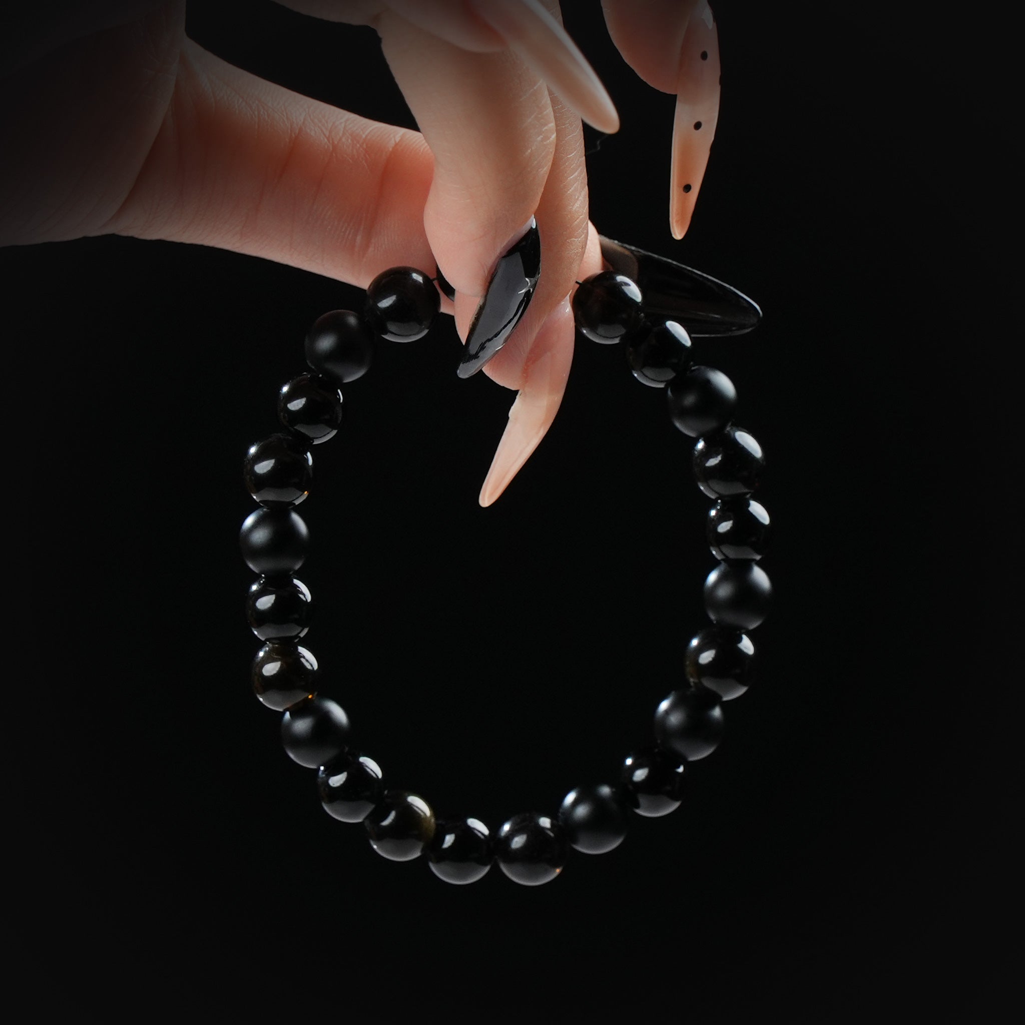 Black obsidian beaded bracelet combining matte and glossy textures, held by hand on black background for protection and grounding.