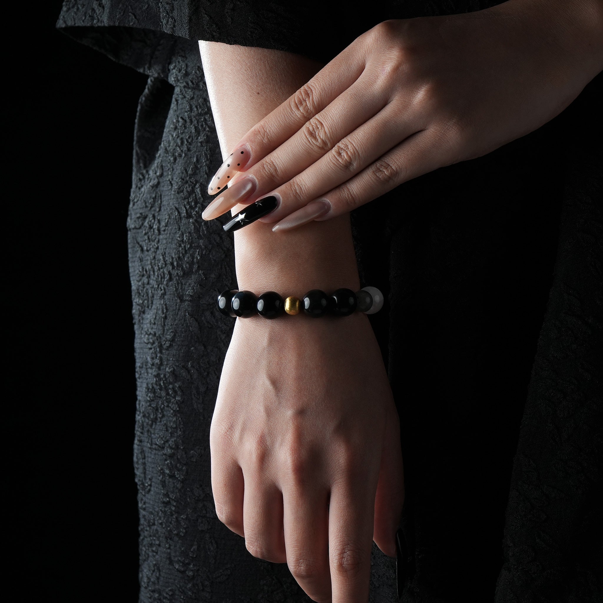 Minimalist bracelet featuring glossy black onyx beads with a single gold bead at the center, worn on a wrist with black textured clothing background.