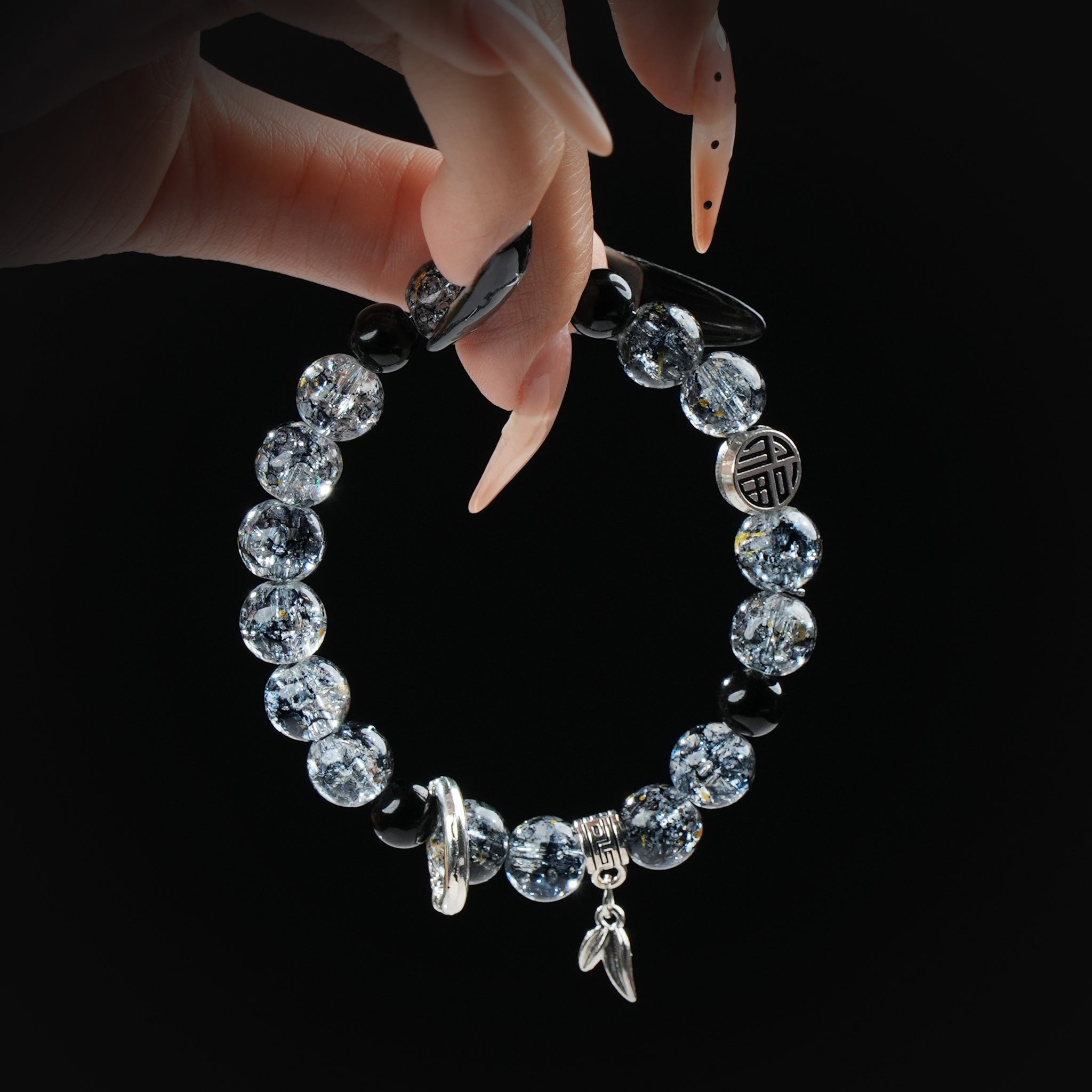 Black rutilated quartz beaded bracelet with silver charms and symbols, held by hand on black background for strength and protection.