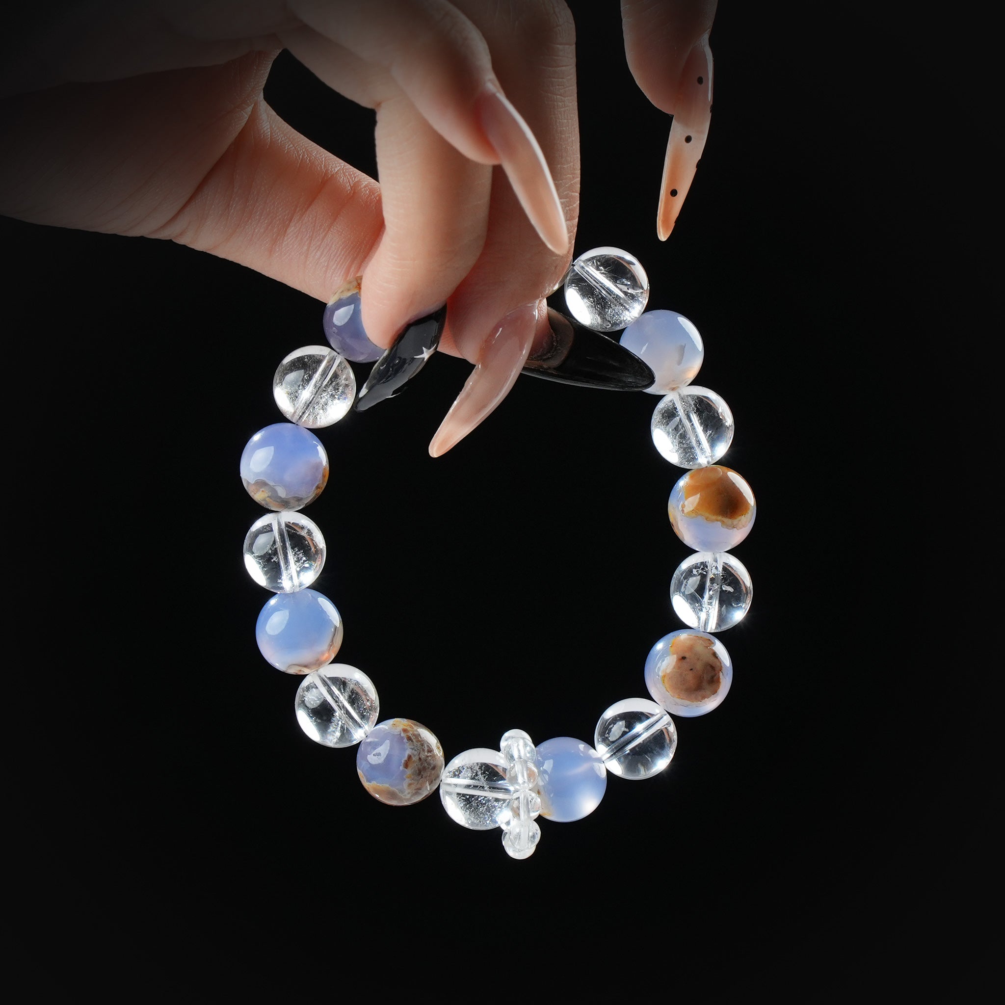 Elegant bracelet featuring alternating blue agate and clear quartz beads with natural patterns, held by hand against a black background.