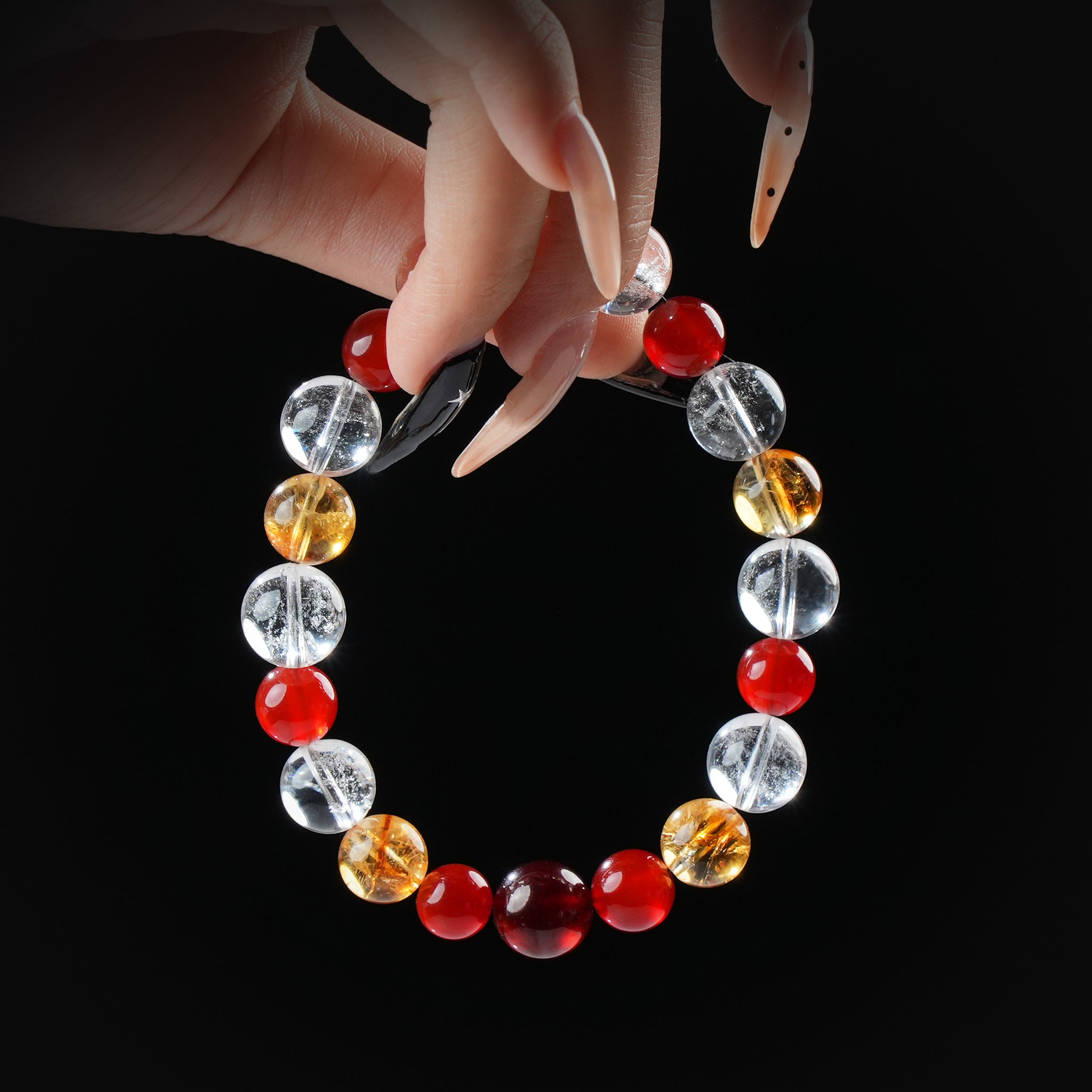 Carnelian, citrine, and clear quartz beaded bracelet held by hand on black background for vitality and abundance.