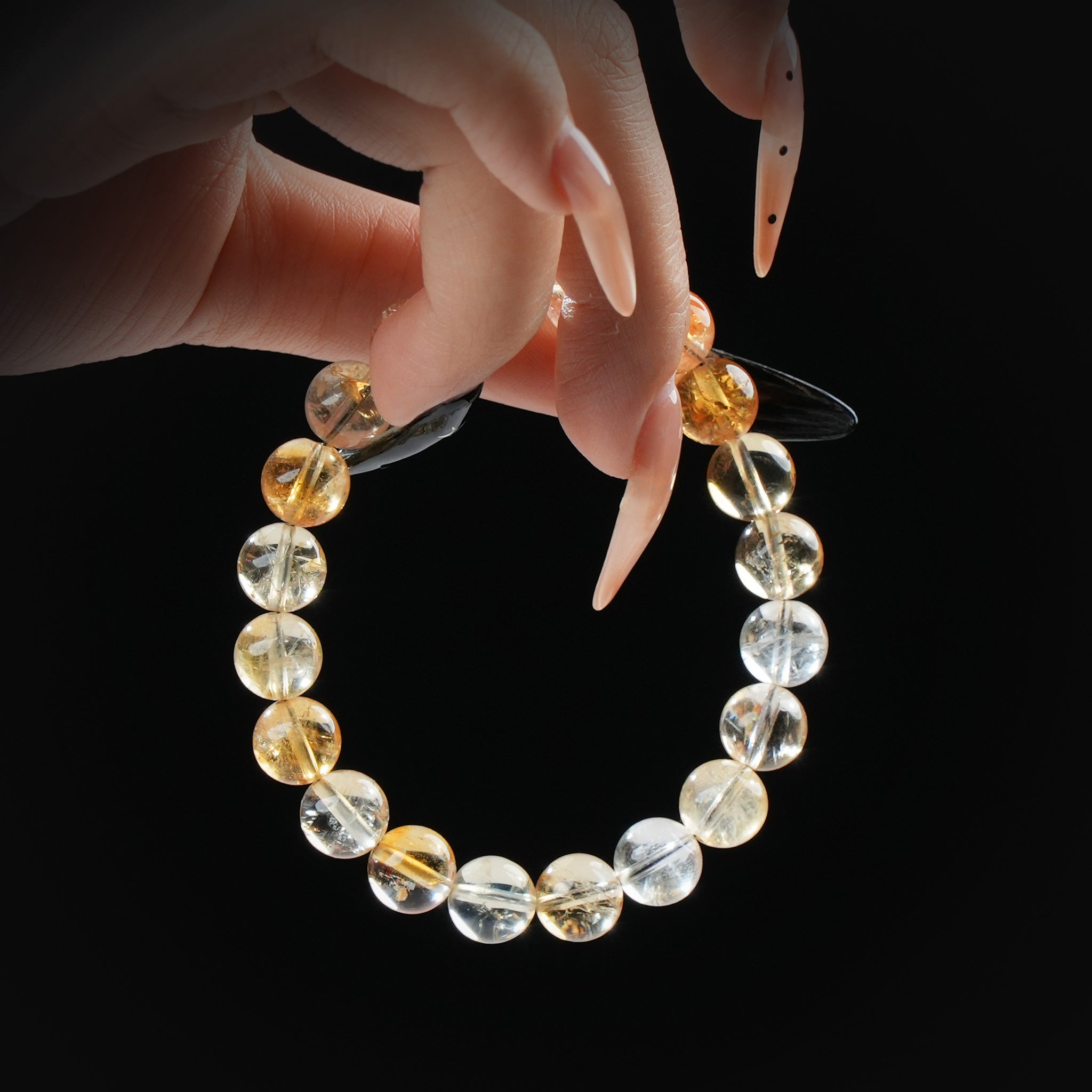 Citrine sunshine beaded bracelet with golden tones, held by hand on black background for abundance and positive energy.
