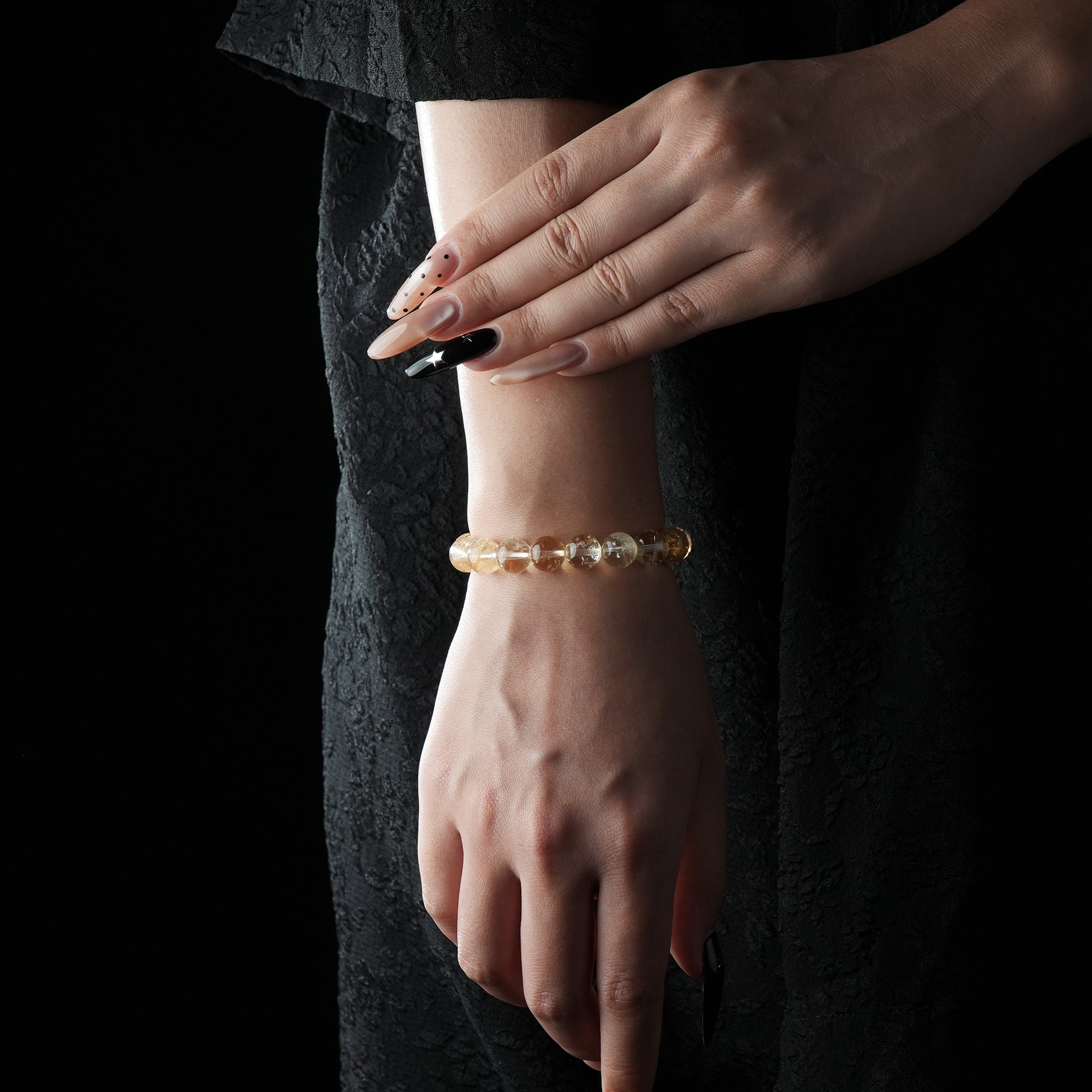 A delicate bracelet made of round citrine crystal beads in golden-yellow tones, worn on the wrist against a black dress background.