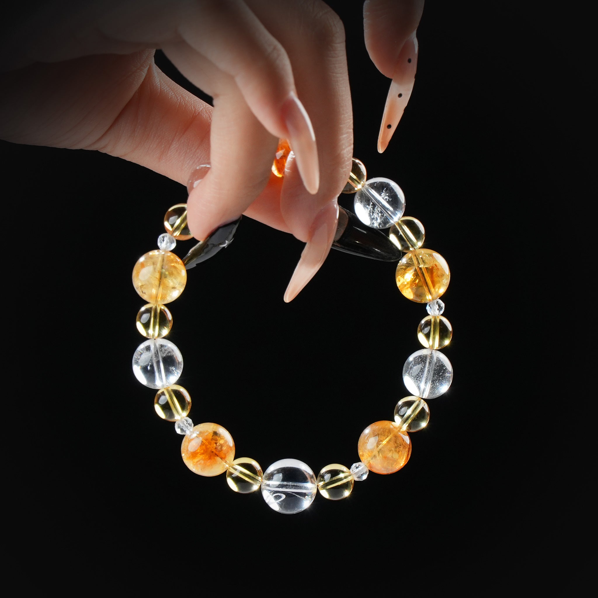 Citrine, golden rutile, and clear quartz beaded bracelet held by hand on black background for abundance and energy amplification.