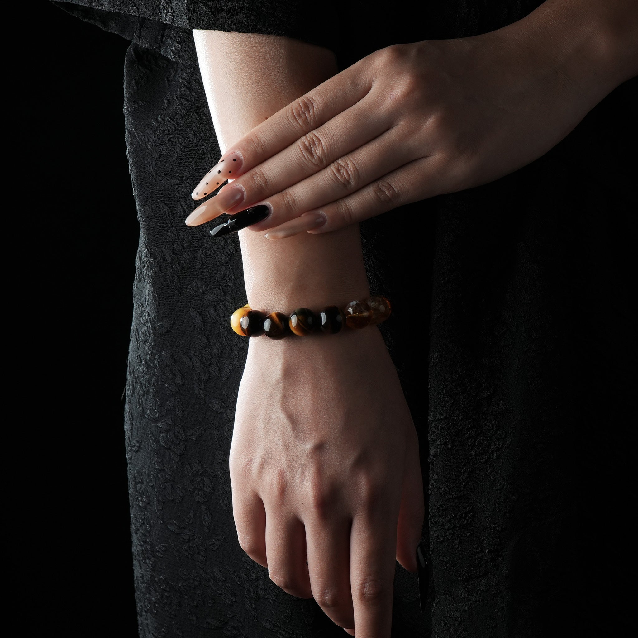 Bracelet composed of citrine, tiger's eye, and white crystal beads, displaying golden, brown, and translucent tones, worn on a wrist against a dark fabric background.