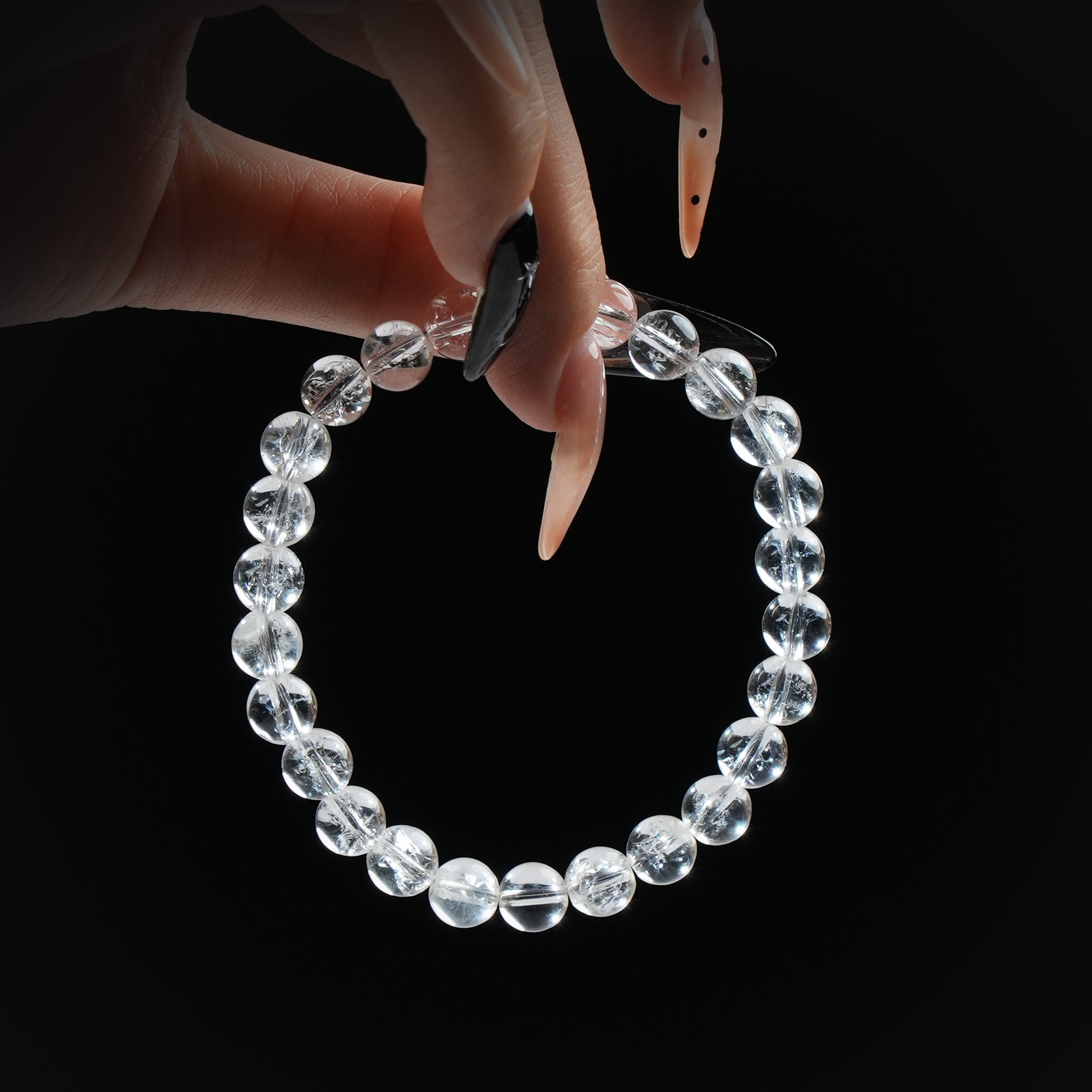 Clear quartz beaded bracelet with highly transparent stones, held by hand on black background, symbolizing clarity and healing.