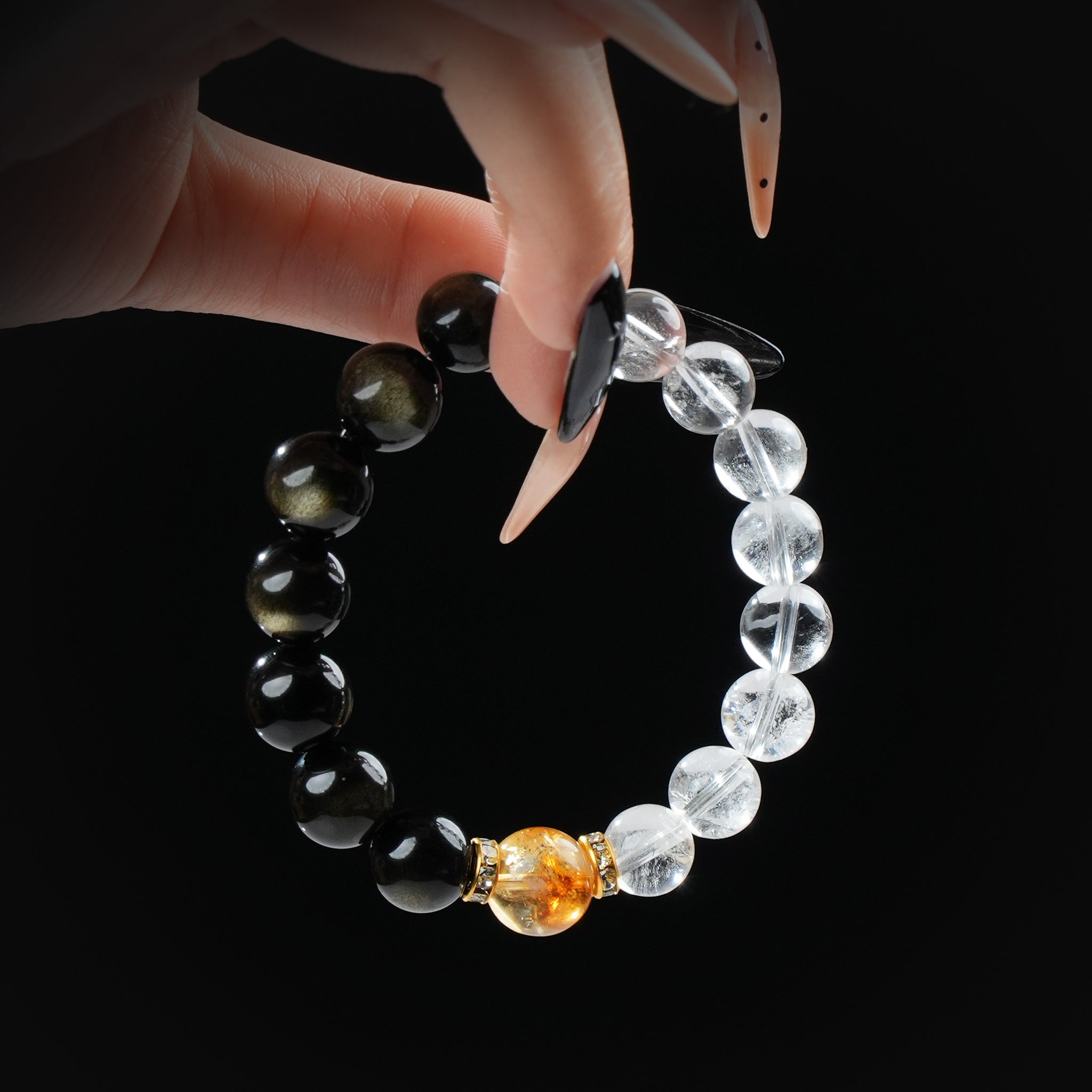 Gold obsidian, citrine, and clear quartz beaded bracelet held by hand against a black background for a bold and energetic look.