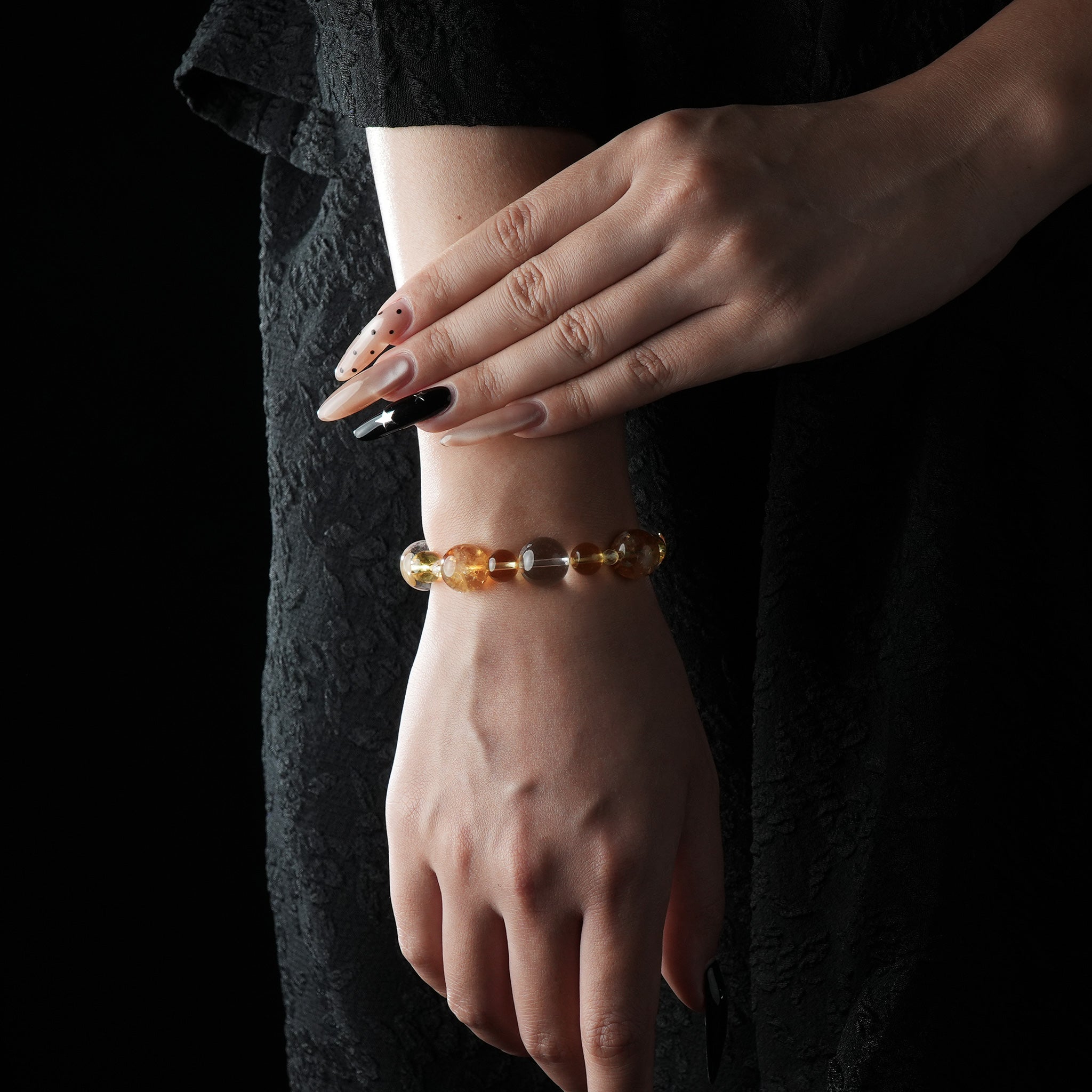 Bracelet made of golden rutilated quartz, citrine, and clear quartz beads, glowing with warm golden tones, worn on a wrist against a black textured background.