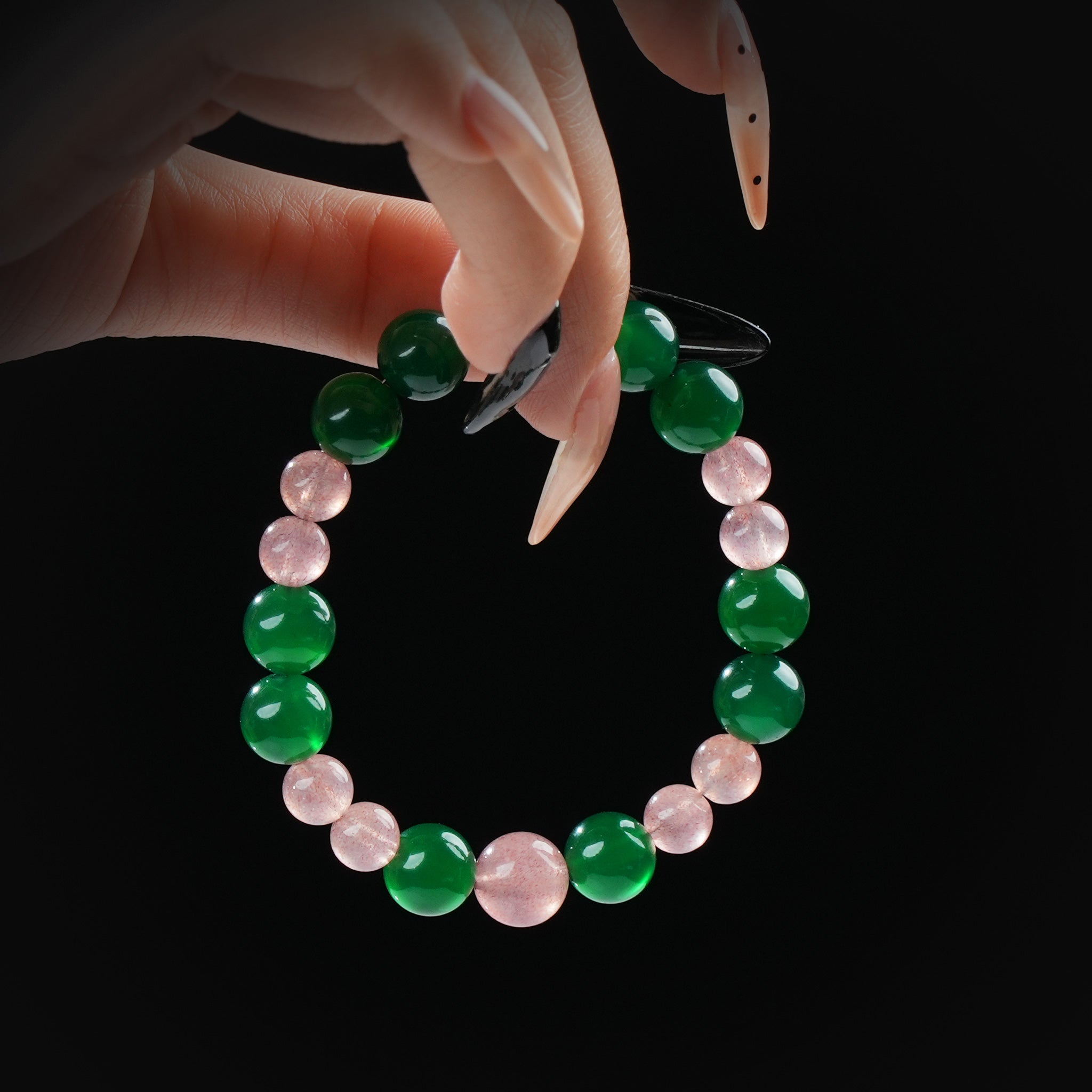 Green agate and rose quartz beaded bracelet held by hand on black background, symbolizing harmony and love.