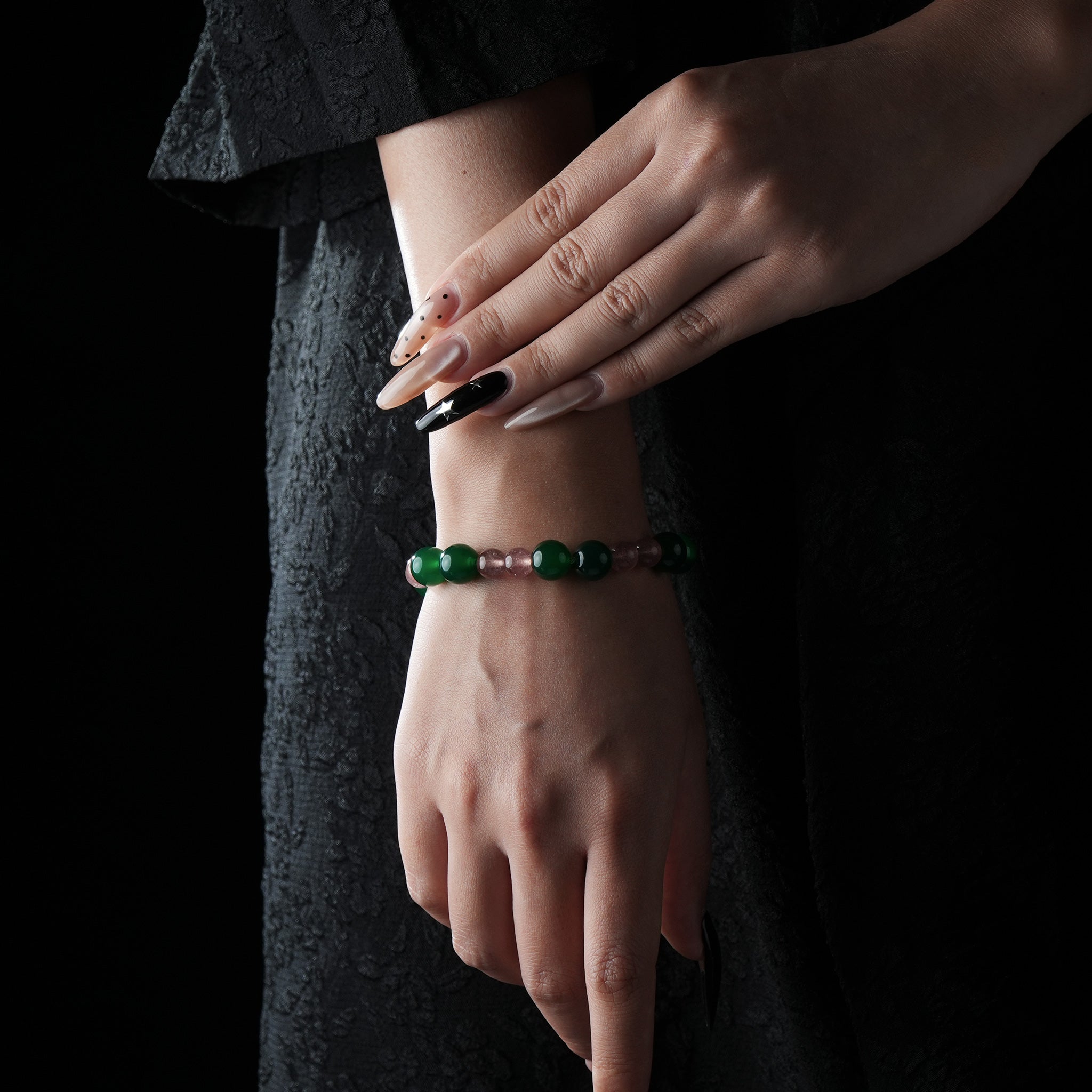 Elegant bracelet with alternating green jade and rose quartz beads, worn on a wrist against a dark textured fabric background.