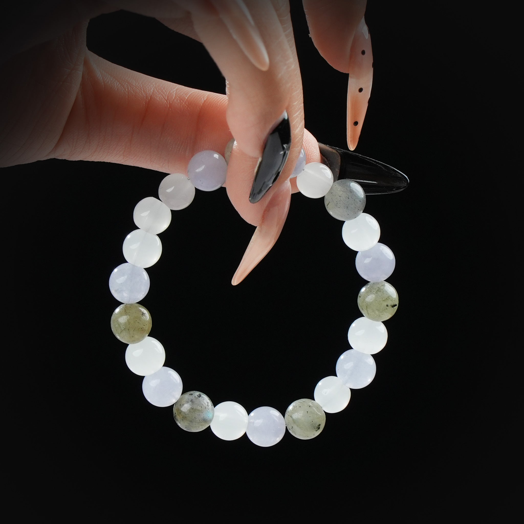 Labradorite, moonstone, and blue lace agate beaded bracelet held by hand on black background for calm, balance, and spiritual insight.