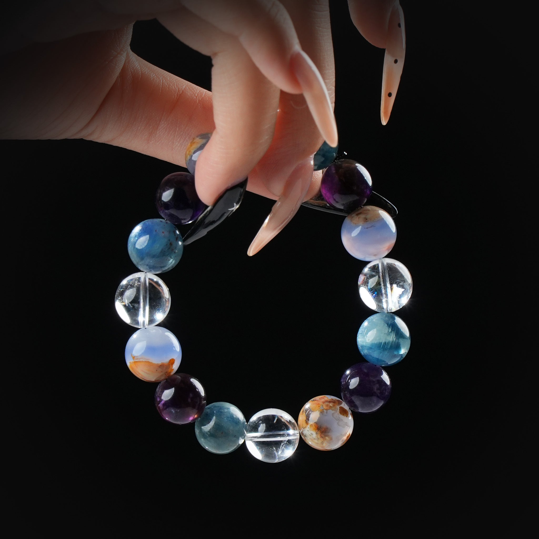 Mixed gemstone and clear quartz beaded bracelet with unique multicolor stones, held by hand on black background for harmony and creative energy.