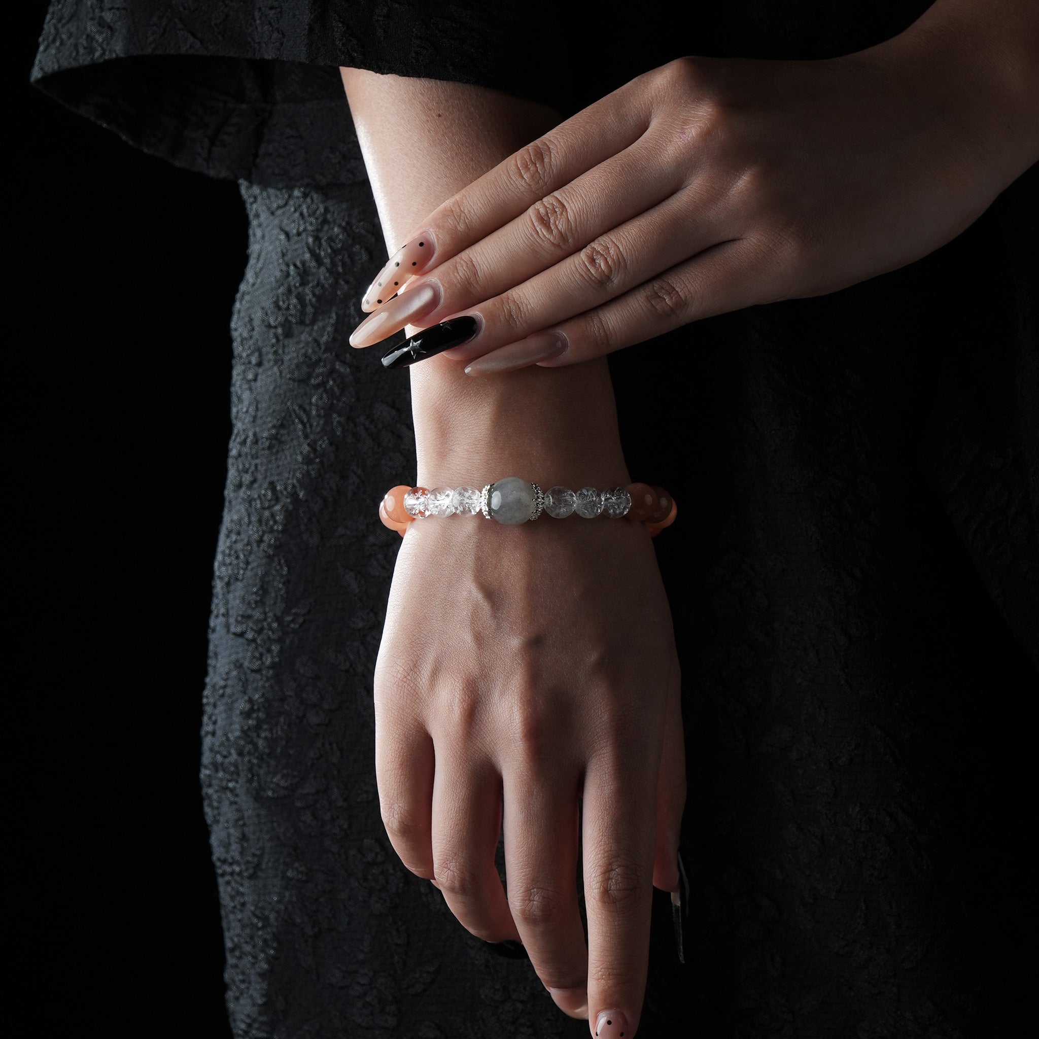 Elegant bracelet featuring a central moonstone, clear quartz beads, and yellow-orange moonstone beads, worn on the wrist against a black lace dress background.