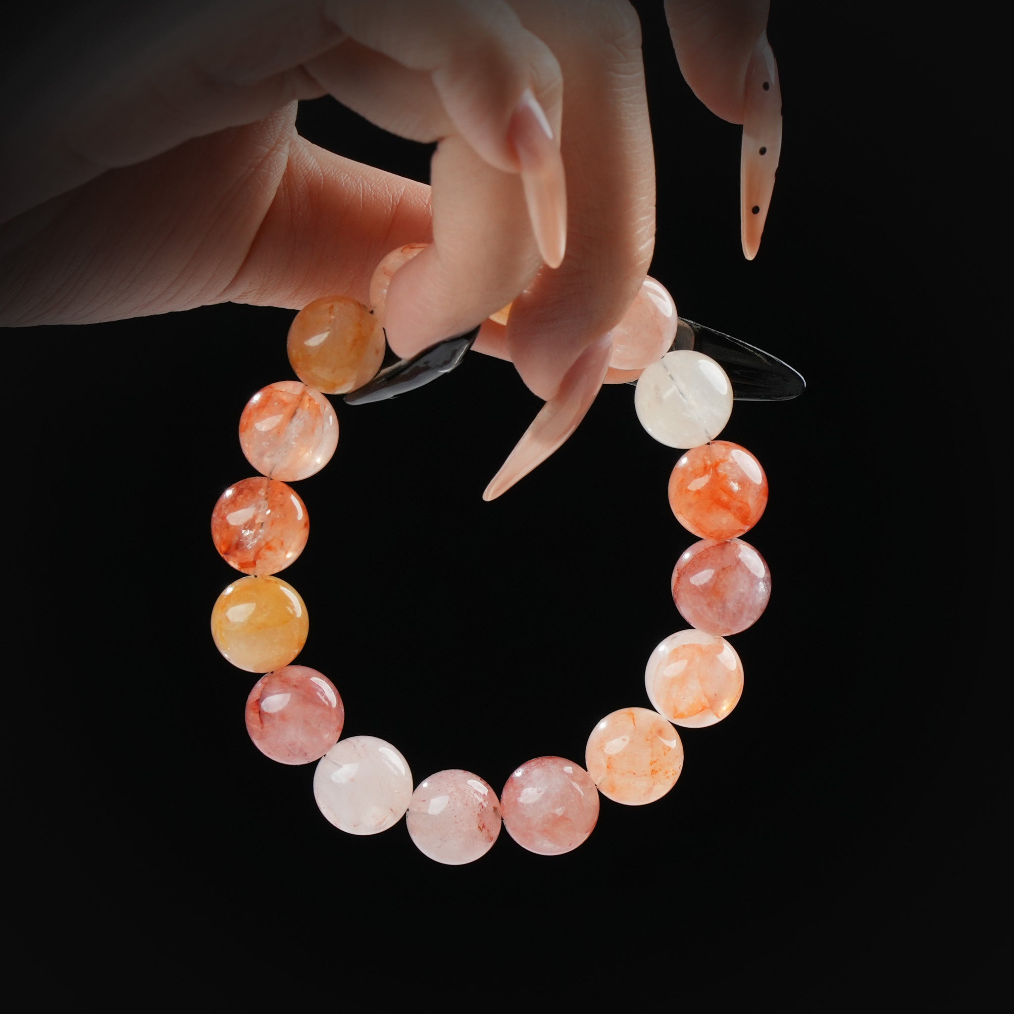 Sunstone and fire quartz beaded bracelet in warm orange and red tones, held by hand on black background for vitality and inner fire.