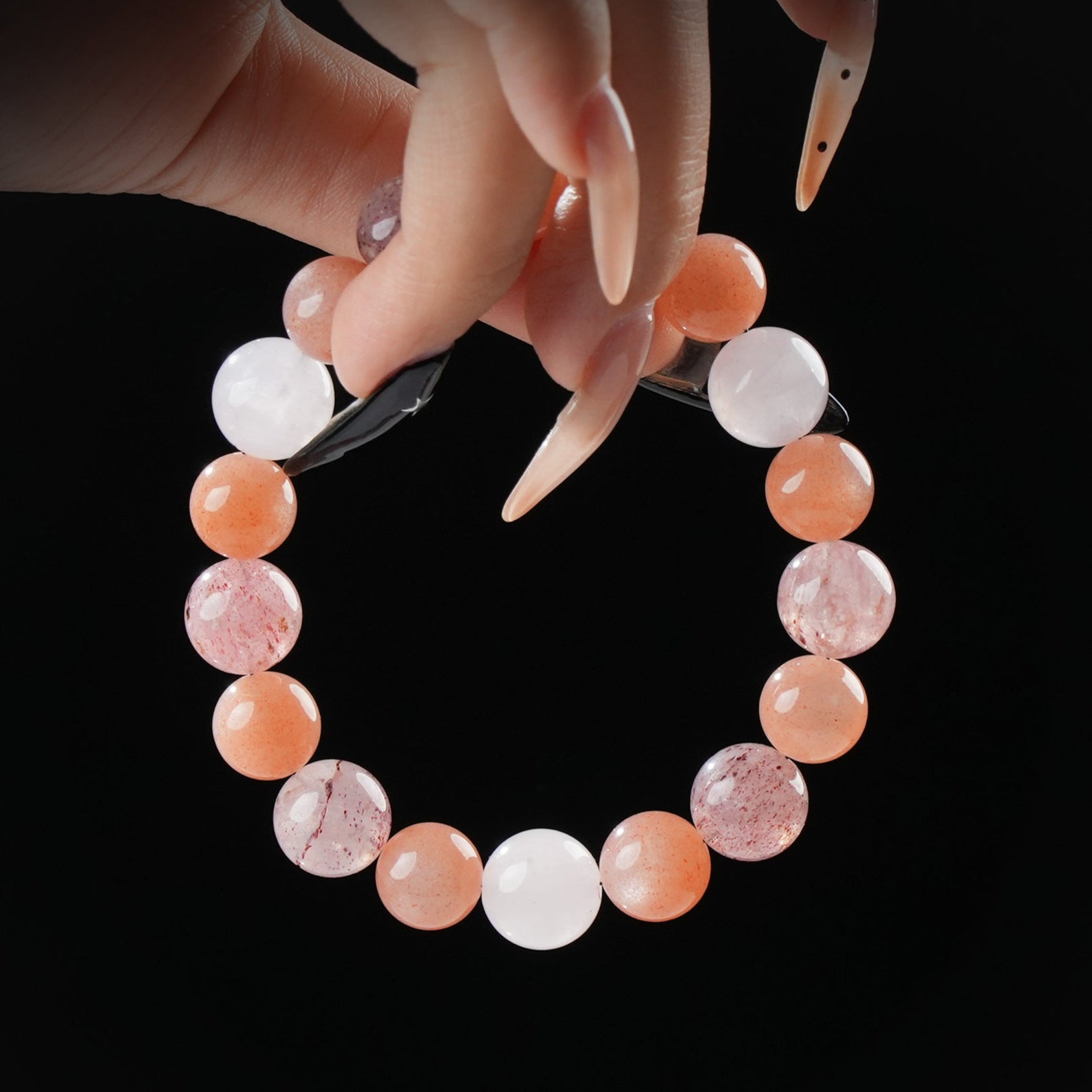 Bright bracelet made of sunstone and moonstone beads in shades of orange, pink, and peach, held by hand against a black background.