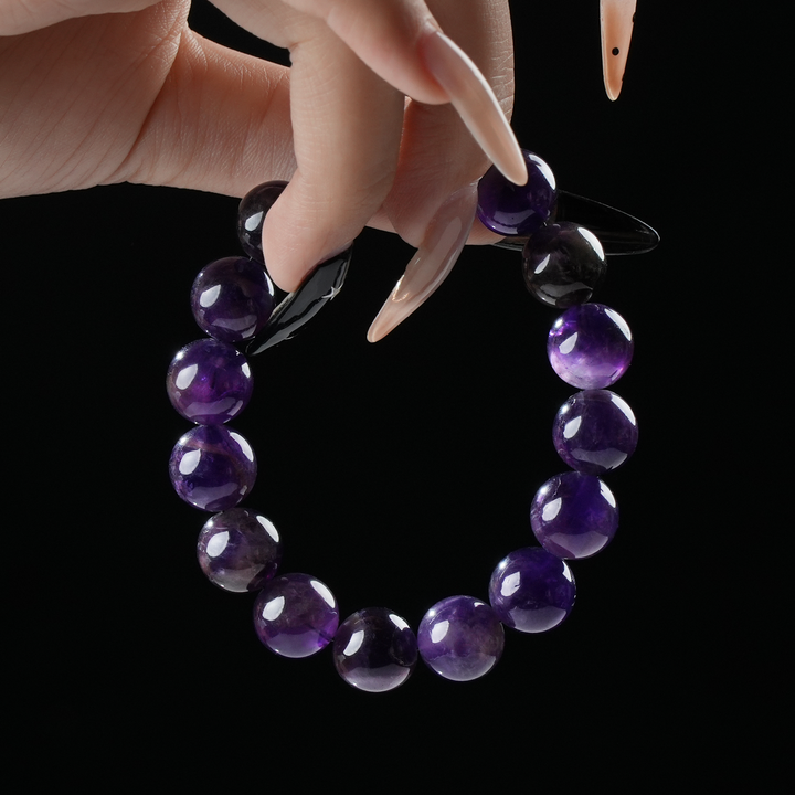 A round bead bracelet made of deep purple crystals held between manicured fingers against a black background.