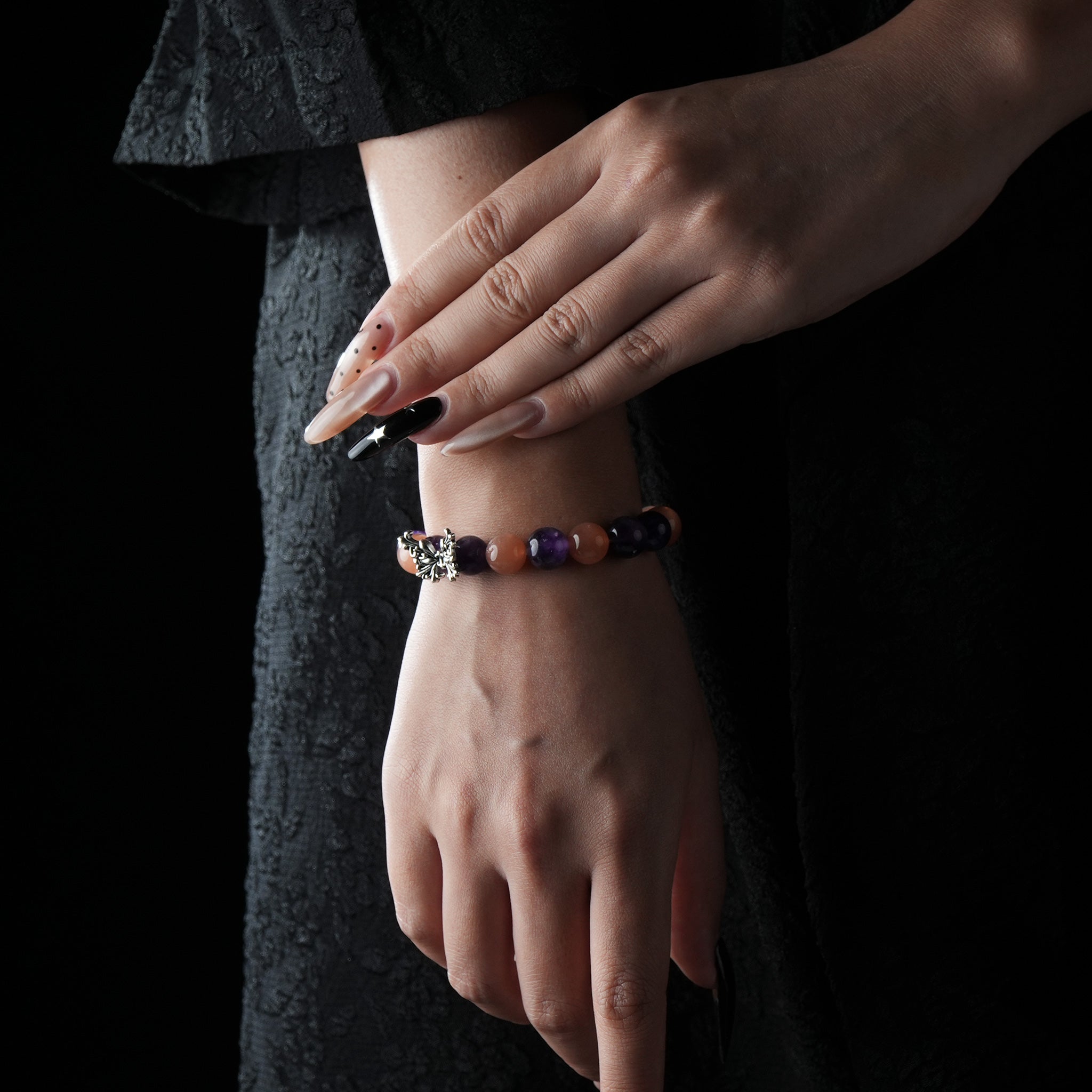 A stylish bracelet featuring alternating purple and orange gemstone beads with a silver butterfly charm, worn on a woman's wrist against a dark background.